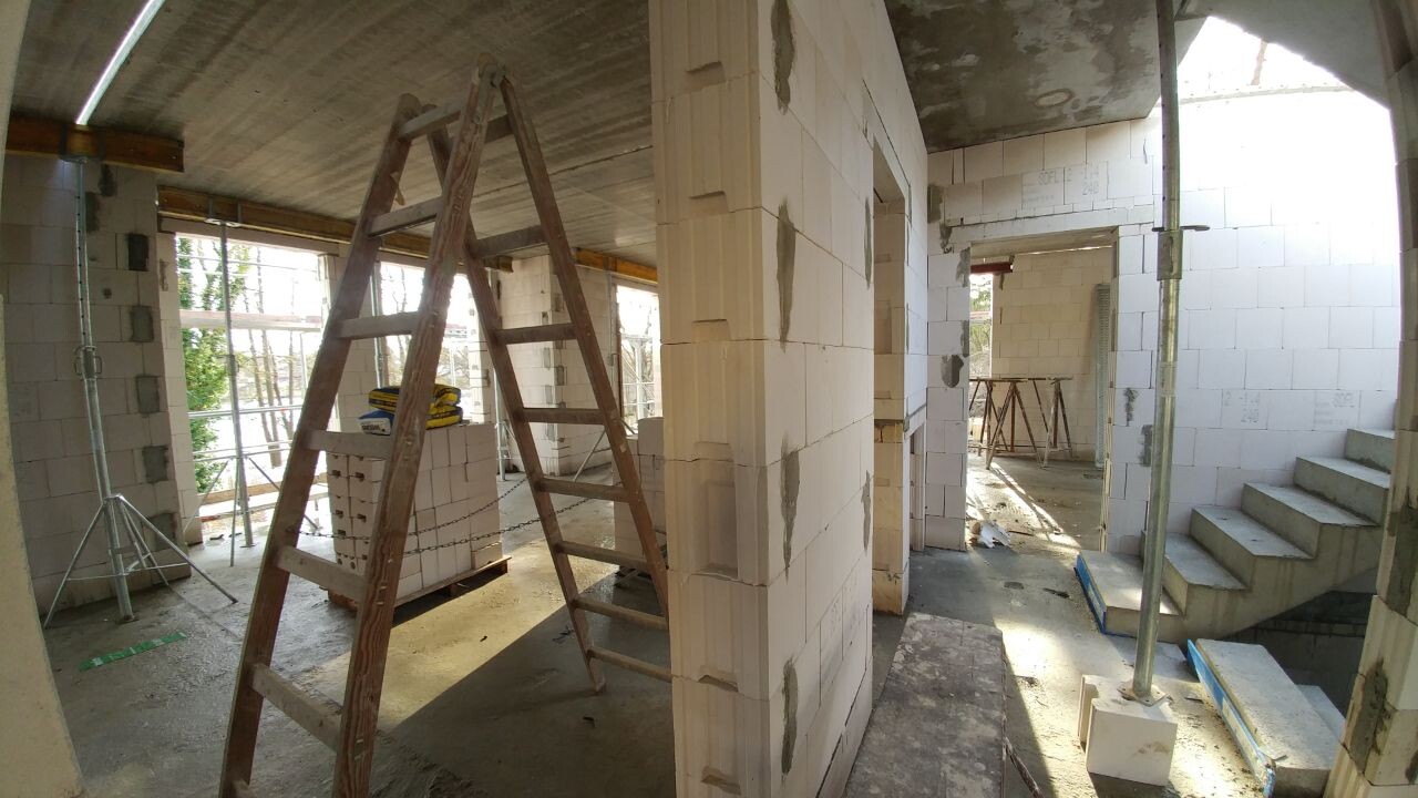 Innenraum einer Baustelle: Holzleiter, weiße Porenbeton-Steine, Treppenstufen, Gerüst