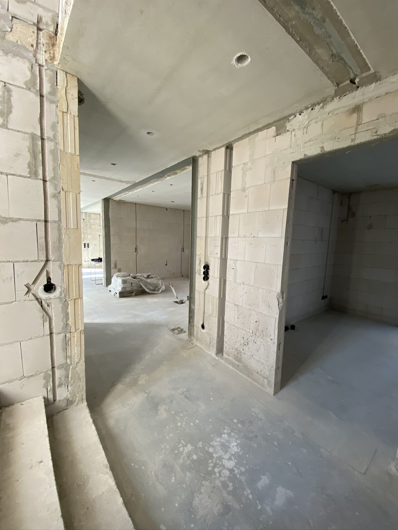 Unfertiger Innenraum eines Bauprojekts: Betonwände, Stützen, Leitungen, Baumaterialien im Zentrum.