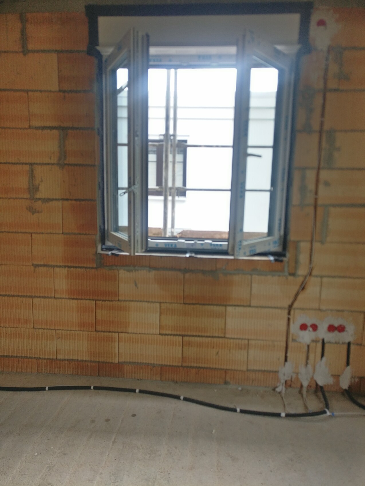 Offenes Fenster in einer rohen Ziegelwand; Kabel am Boden, Baustelle im Innenraum.