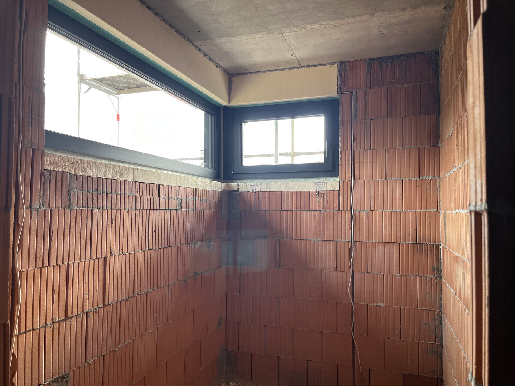 Rohbau-Innenraum mit roten Ziegelwänden, Fenster und unfertige Decke