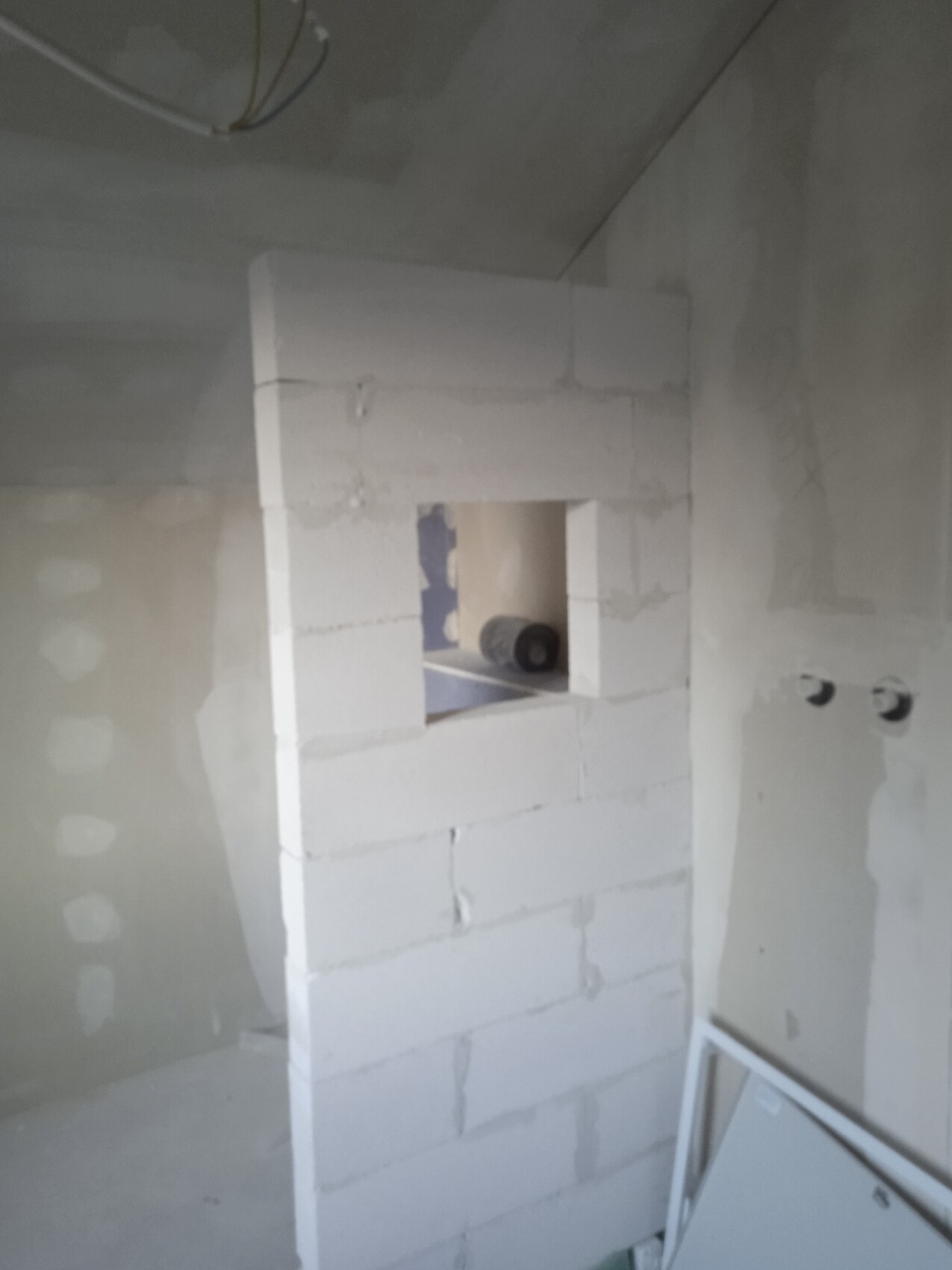 Rohbau-Innenraum: Porenbetonblockwand mit Fensteröffnung und Bauinstallationen sichtbar