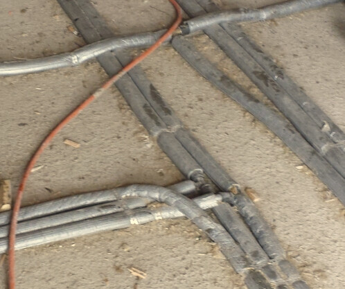 Baustellenboden mit Kabelkanälen und Metallrohren auf Sandboden.