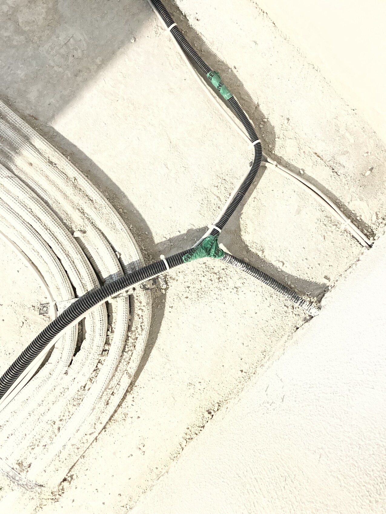 Baustelle: schwarze Kabelkanäle kreuzen rauen Beton, grüne Klebebänder sichern Verbindungen.
