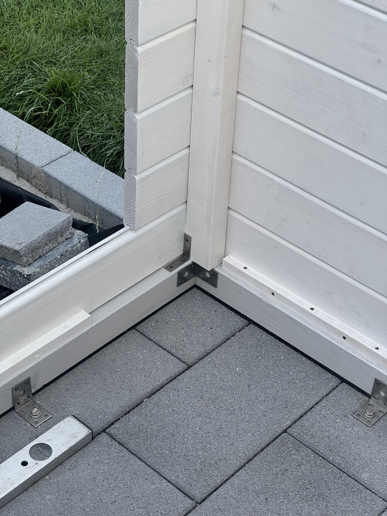 Außenwand Ecke mit heller Holzverkleidung, Eckpfosten, Metallwinkel und grauen Pflasterplatten