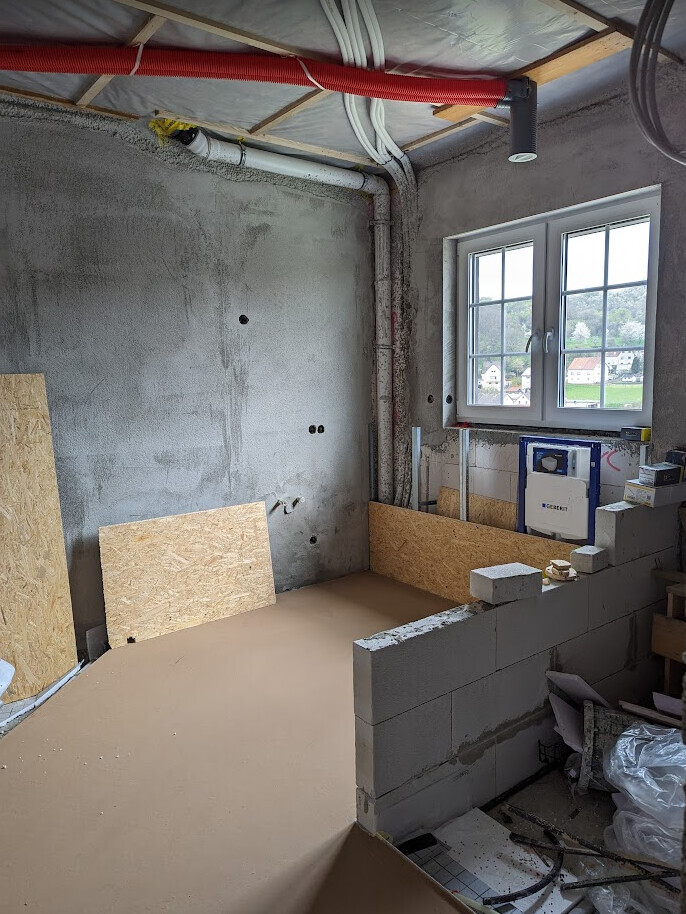 Rohbaustelle: Badezimmerunterbau mit Rohren, OSB-Platten, Geberit-Spülkasten und Fenster.