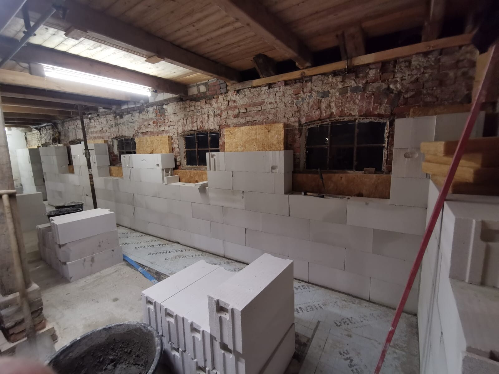 Keller: Neue Innenwand aus Porenbetonblöcken entsteht; dahinter Backsteinwand und Holzbalkendecke sichtbar.