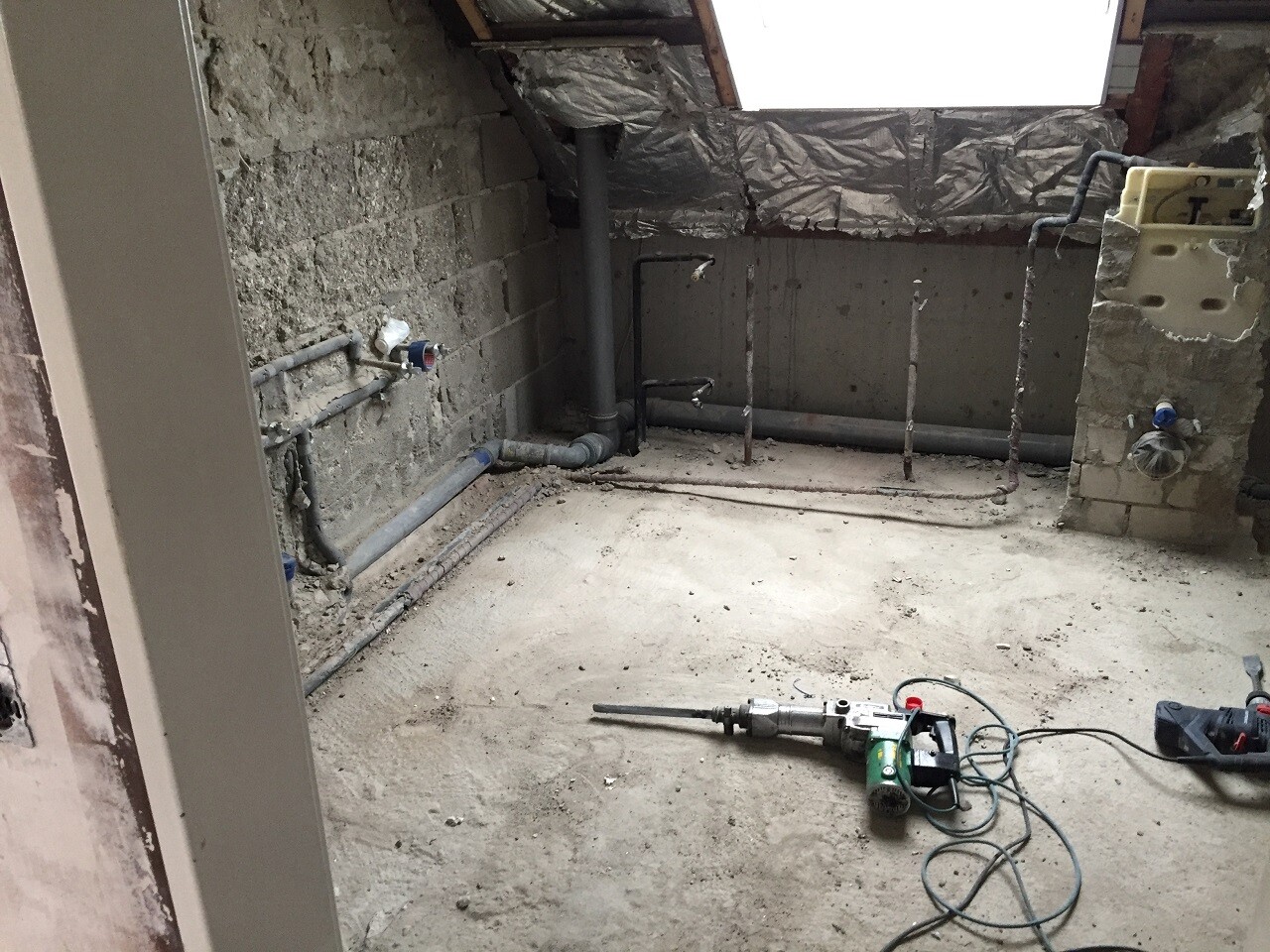 Baustelle im Keller mit Rohbauwänden, Sanitärleitungen und Werkzeug auf dem Boden