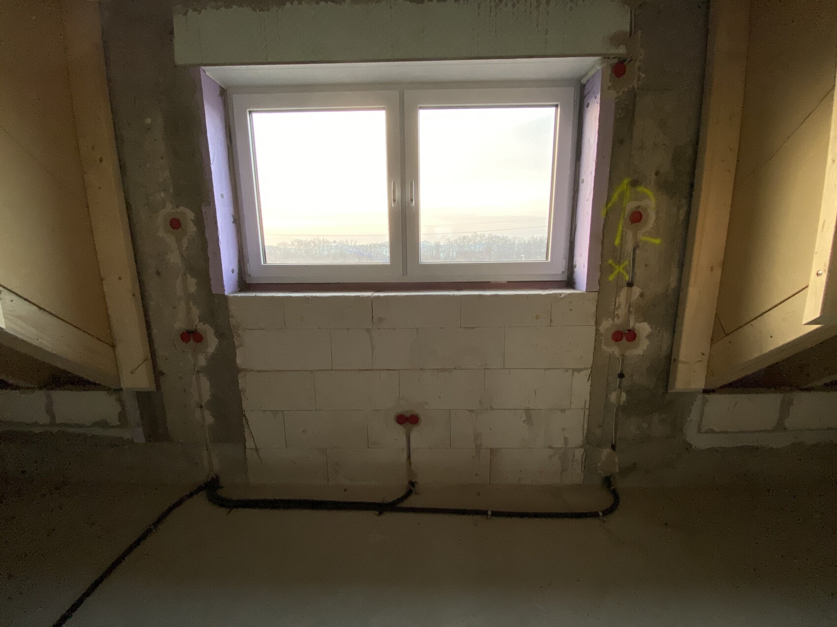 Unfertiger Kellerraum mit Fenster, Betonwänden, roten Steckdosen und Kabeln am Boden.