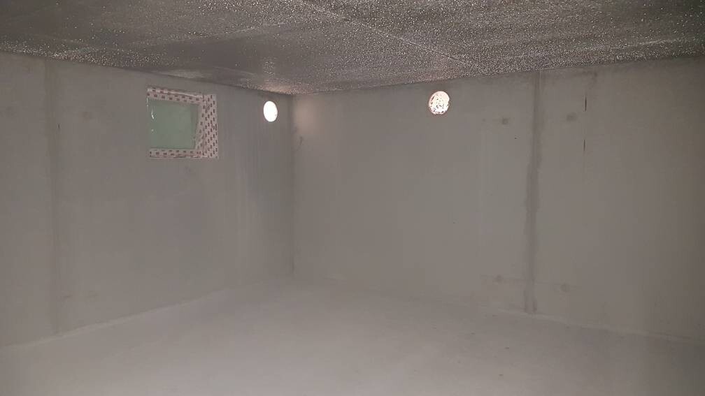 Leerer, grauer Betonraum mit runden Lüftungsöffnungen in der Wand und kleinem Fenster.