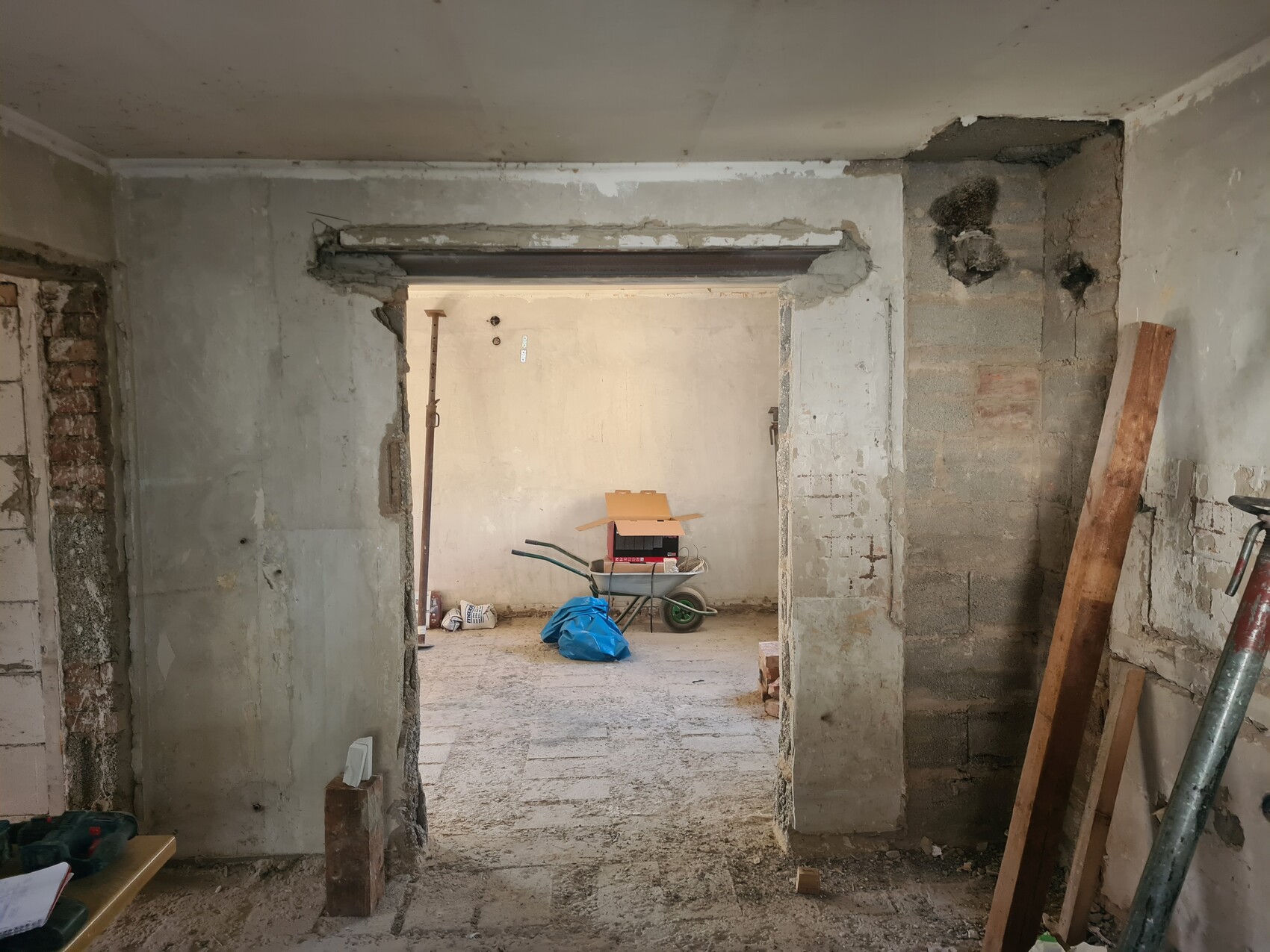 Rohbauraum im Keller, Türöffnung; Werkzeuge, Kartons, blauer Sack und Holzlatten liegen herum.