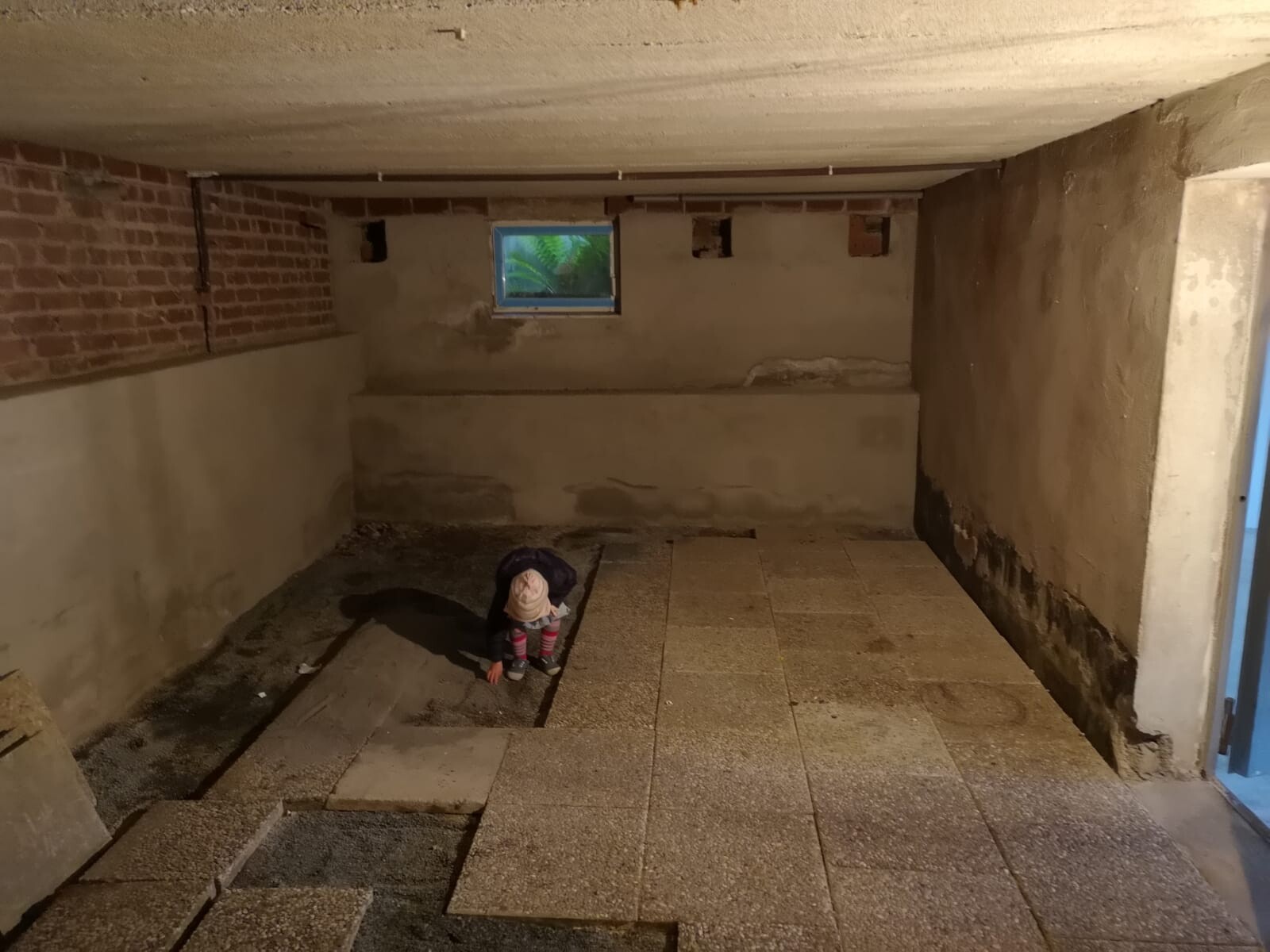 Kellerraum im Rohbau mit Betonwänden, Fliesenboden und kleinem Fenster