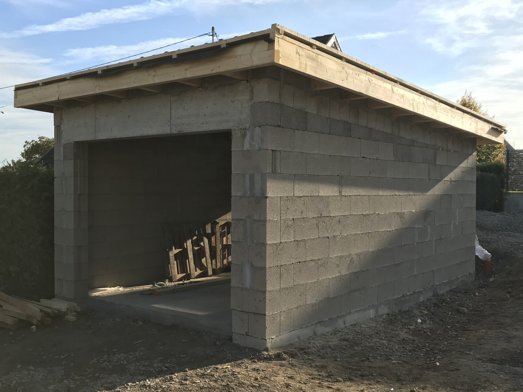 Neubau aus Betonblock mit offener Garagenfront; Holzbalken-Dach auf Baustelle.