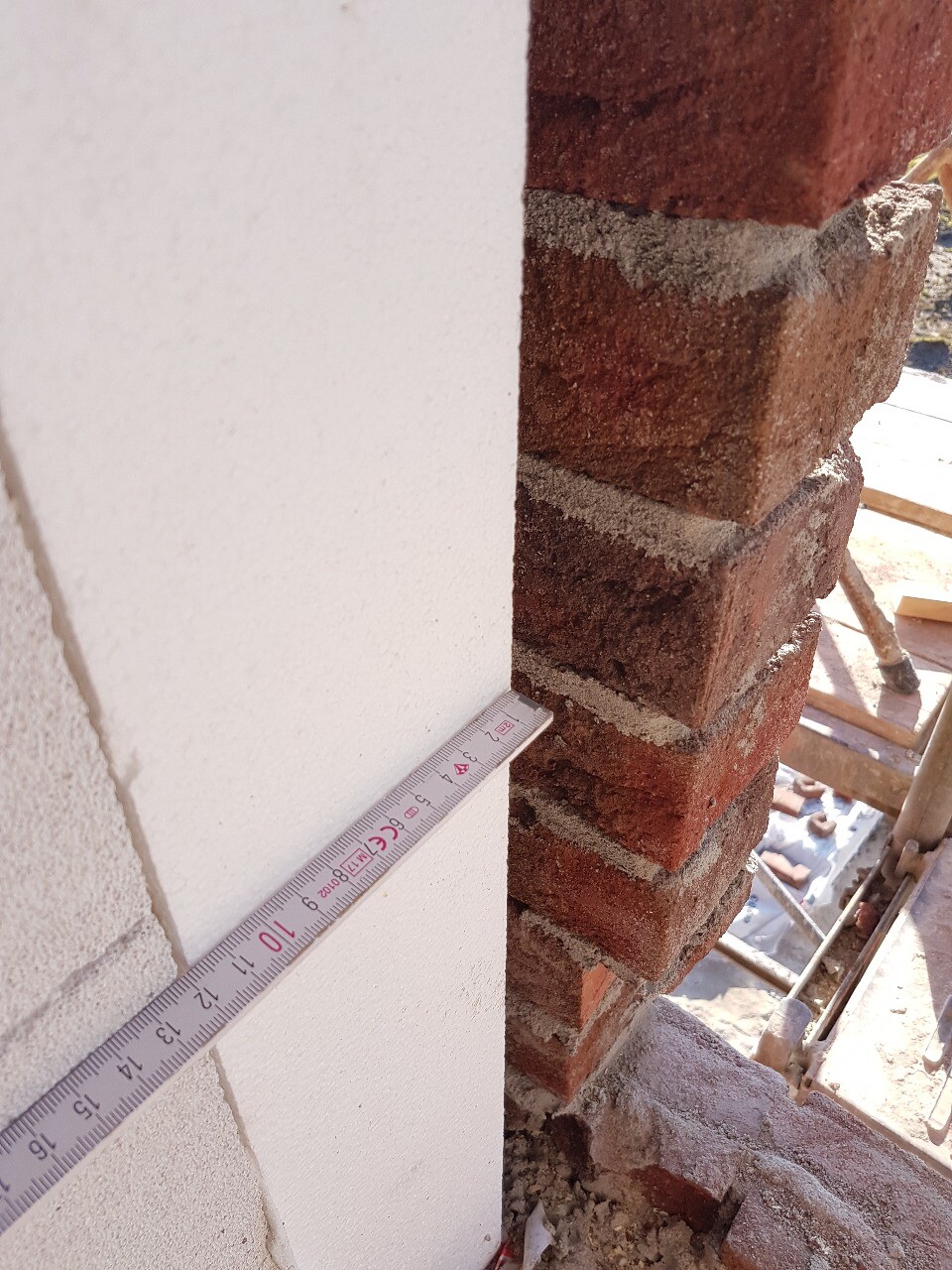 Rohbau: Ziegelwand im Bau mit Messband und Gerüst im Hintergrund