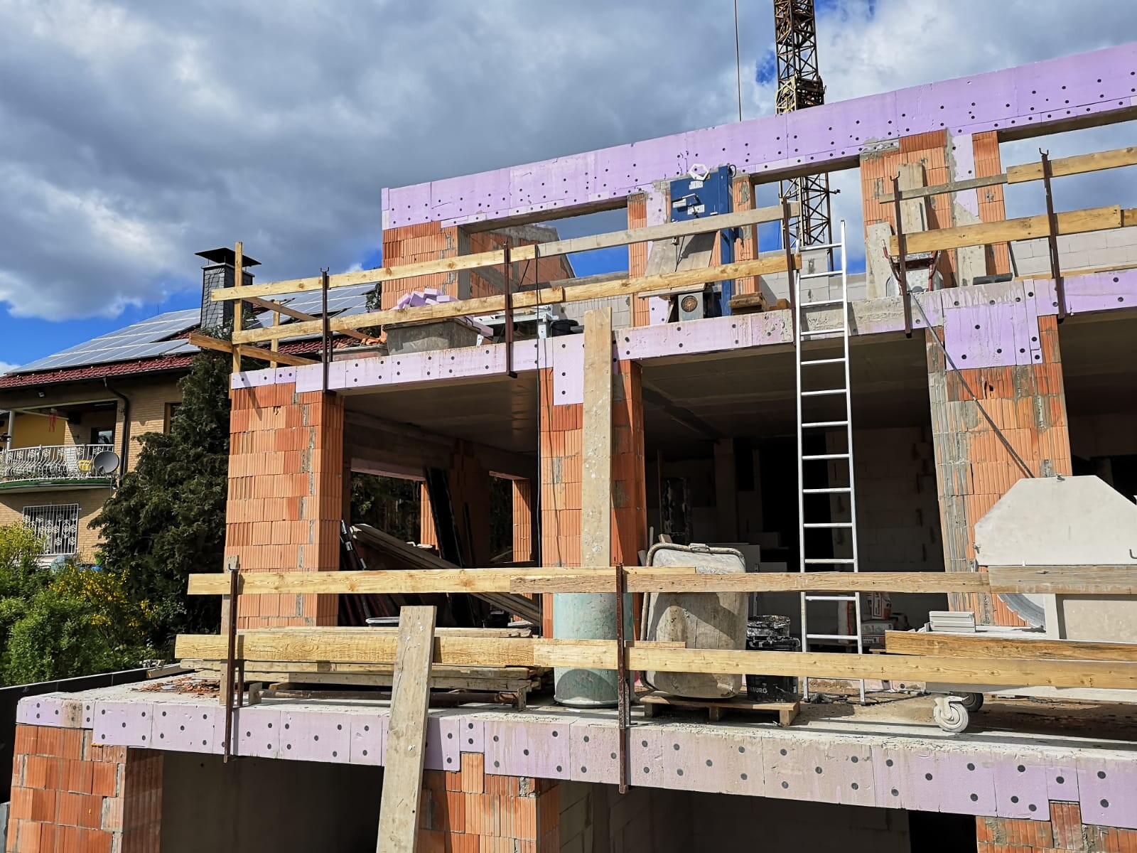 Rohbau eines mehrstöckigen Hauses mit Holzgeländer, Leiter, Ziegeln und Dämmplatten