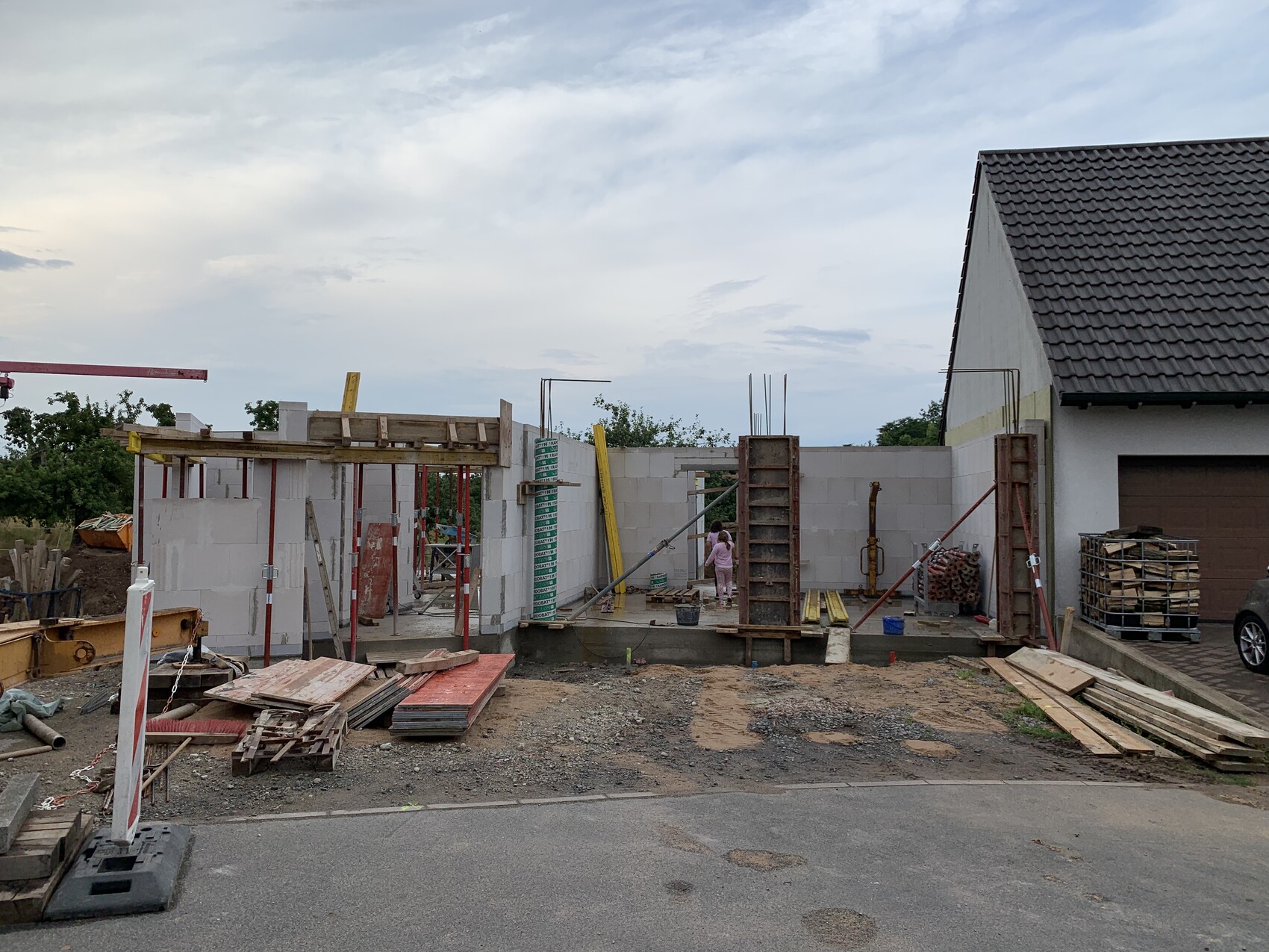 Baustelle vor Einfamilienhaus: unfertige Mauer, Gerüste, Holzplanken; Mädchen in Rosa.