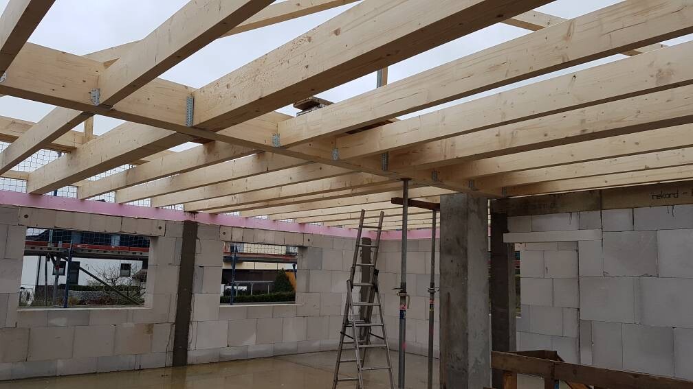 Baustelle: Holzbalkendecke, Betonwände, Leiter und Stützen, Fensteröffnungen.