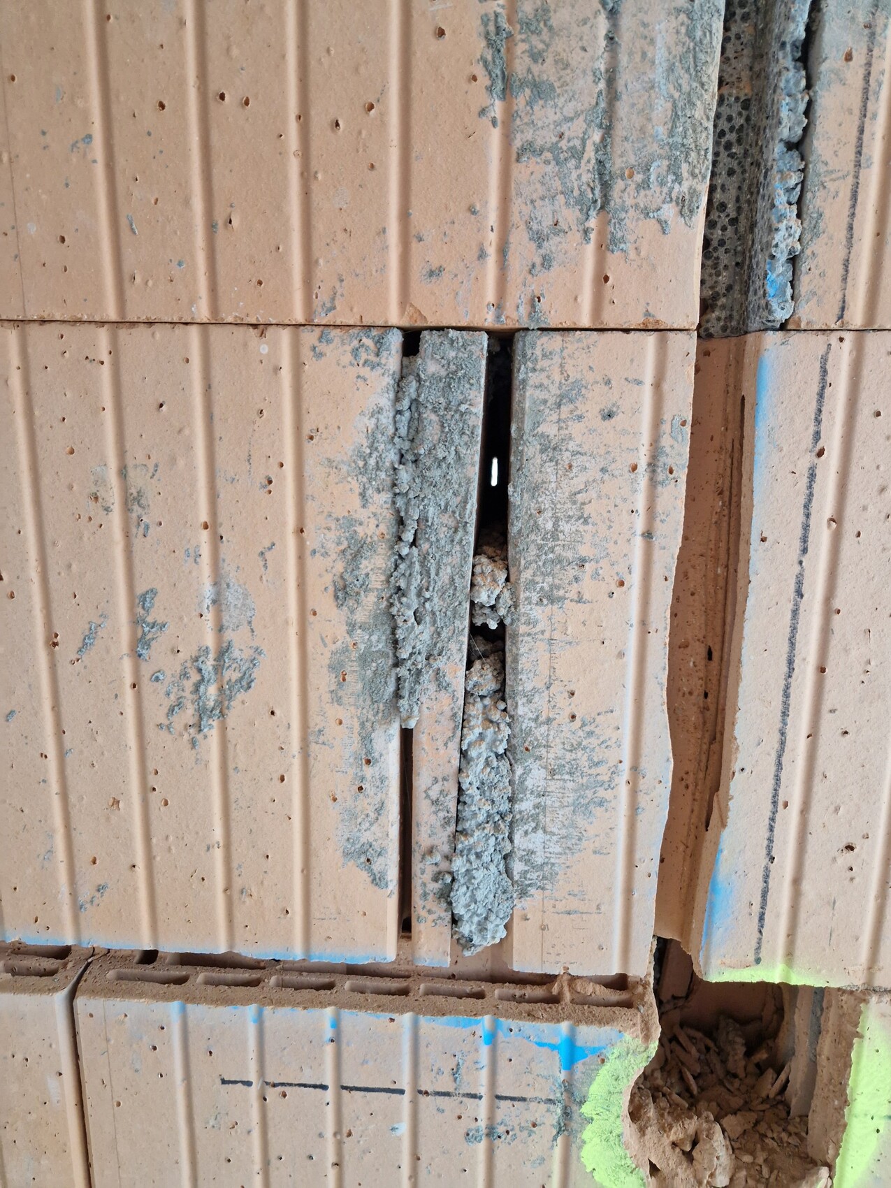 Nahaufnahme einer beschädigten Ziegelwand mit vertikalem Spalt, Zementmörtel und Farbspritzern.