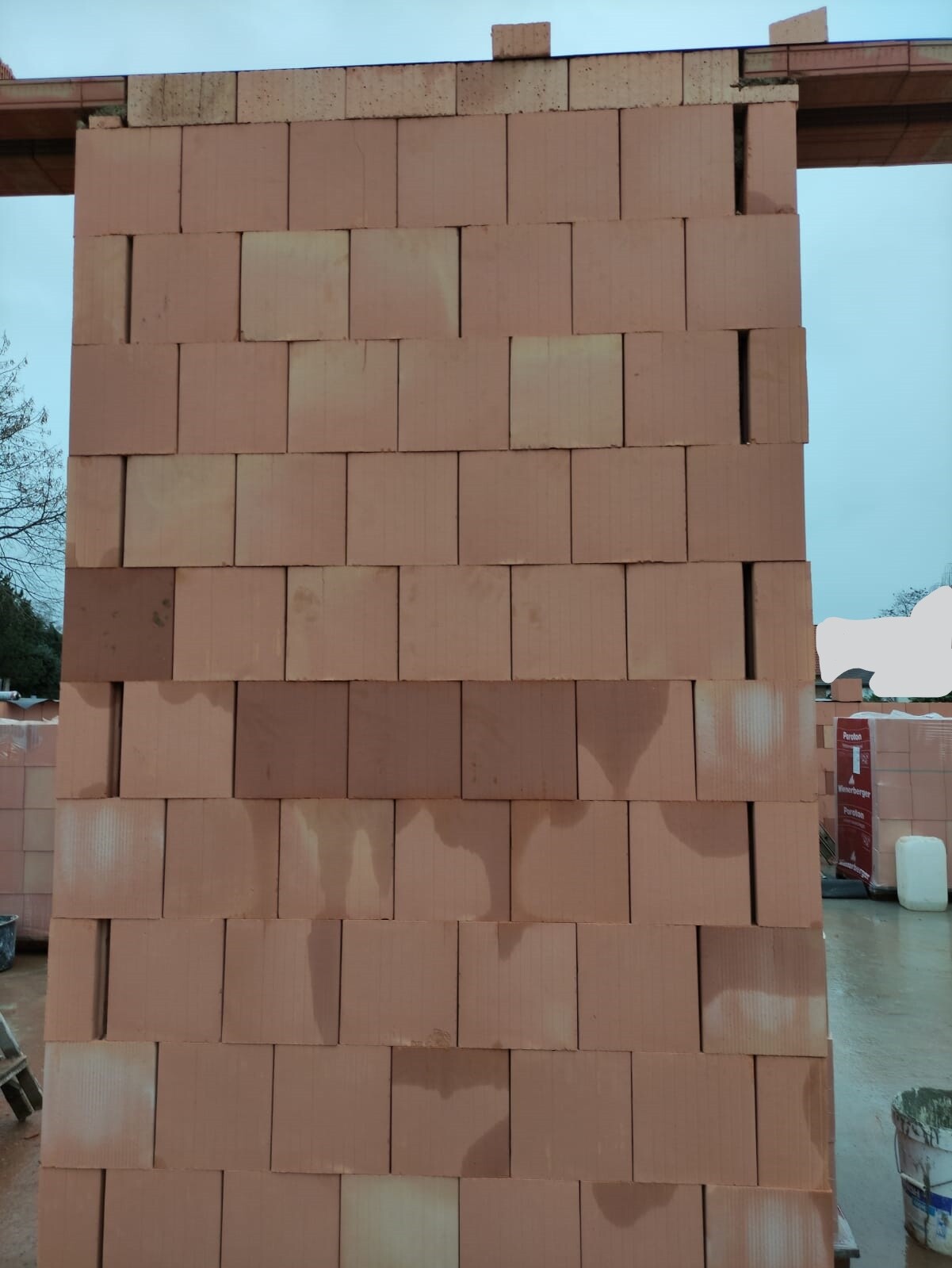 Hohe Backsteinmauer aus roten Steinen auf einer Baustelle, unfertige Ziegelwand.
