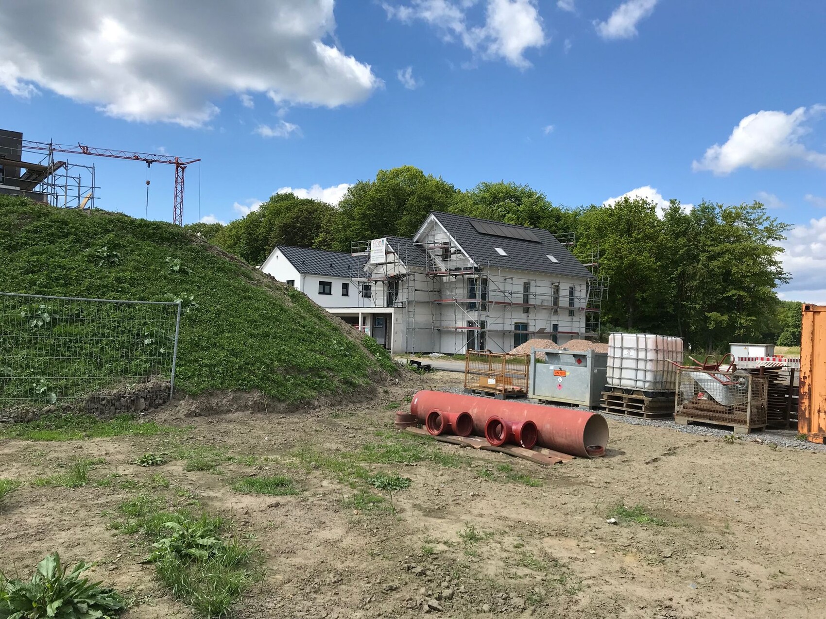 Baustelle: weißes Haus mit Gerüst, Rohre, Paletten und Container.