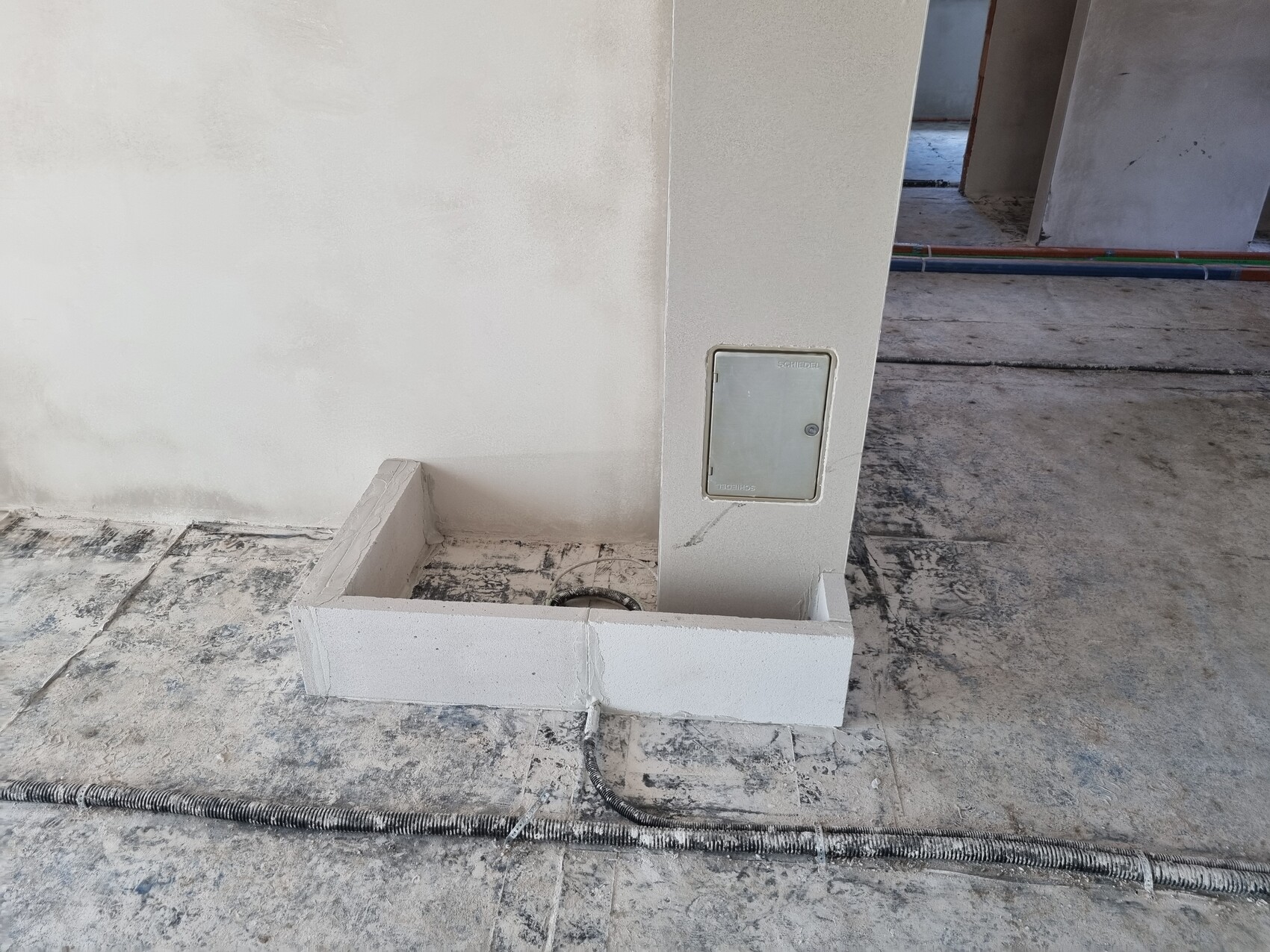 Innenraum einer Baustelle: Betonstütze mit Metall-Wartungskasten, Kabelschlauch am Boden.