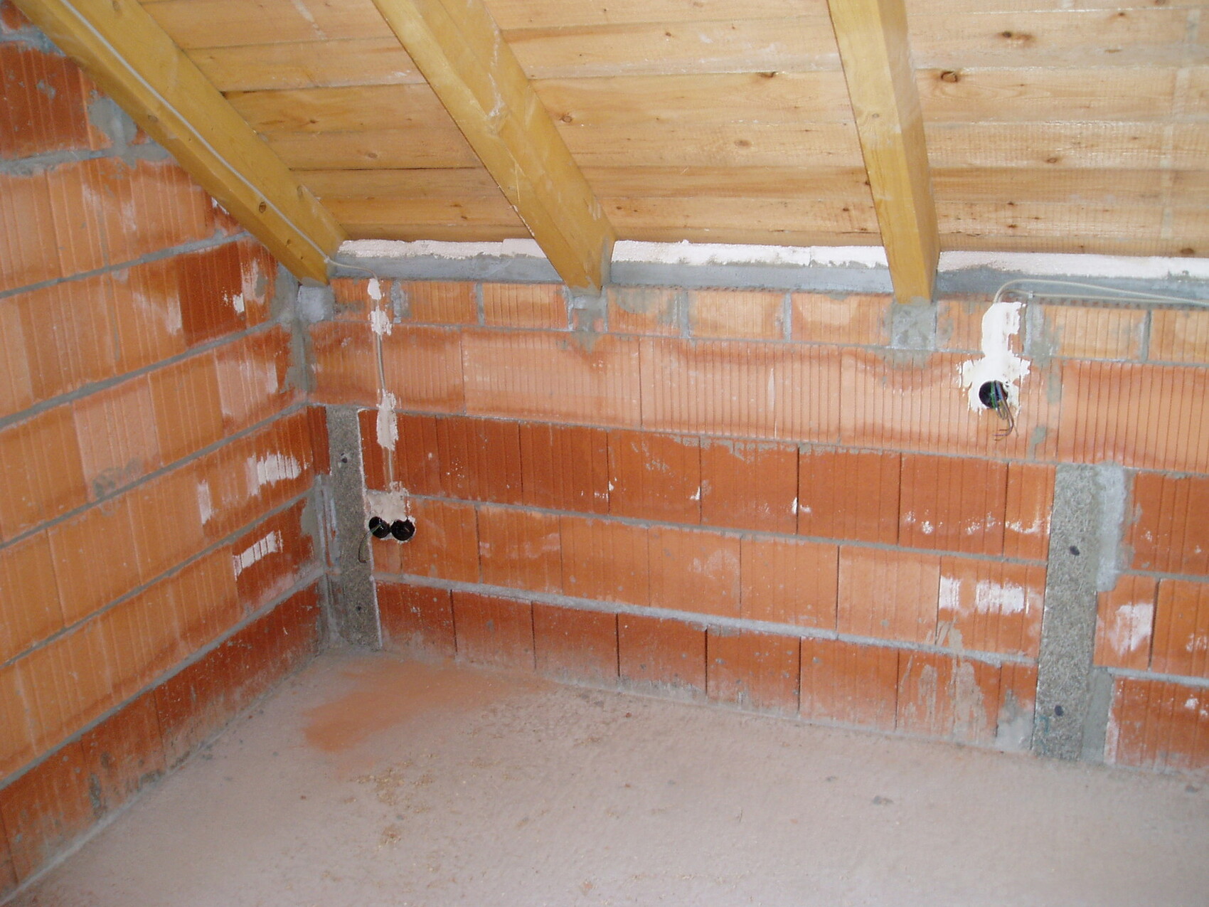 Unverputzter Innenraum im Rohbau mit Ziegelwänden, Dachstuhl und sichtbaren Leitungen.