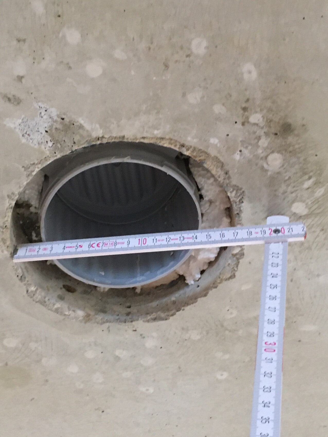 Rundes PVC-Rohr in einer Betonbodenöffnung, Messband zeigt Durchmesser des Lochs.