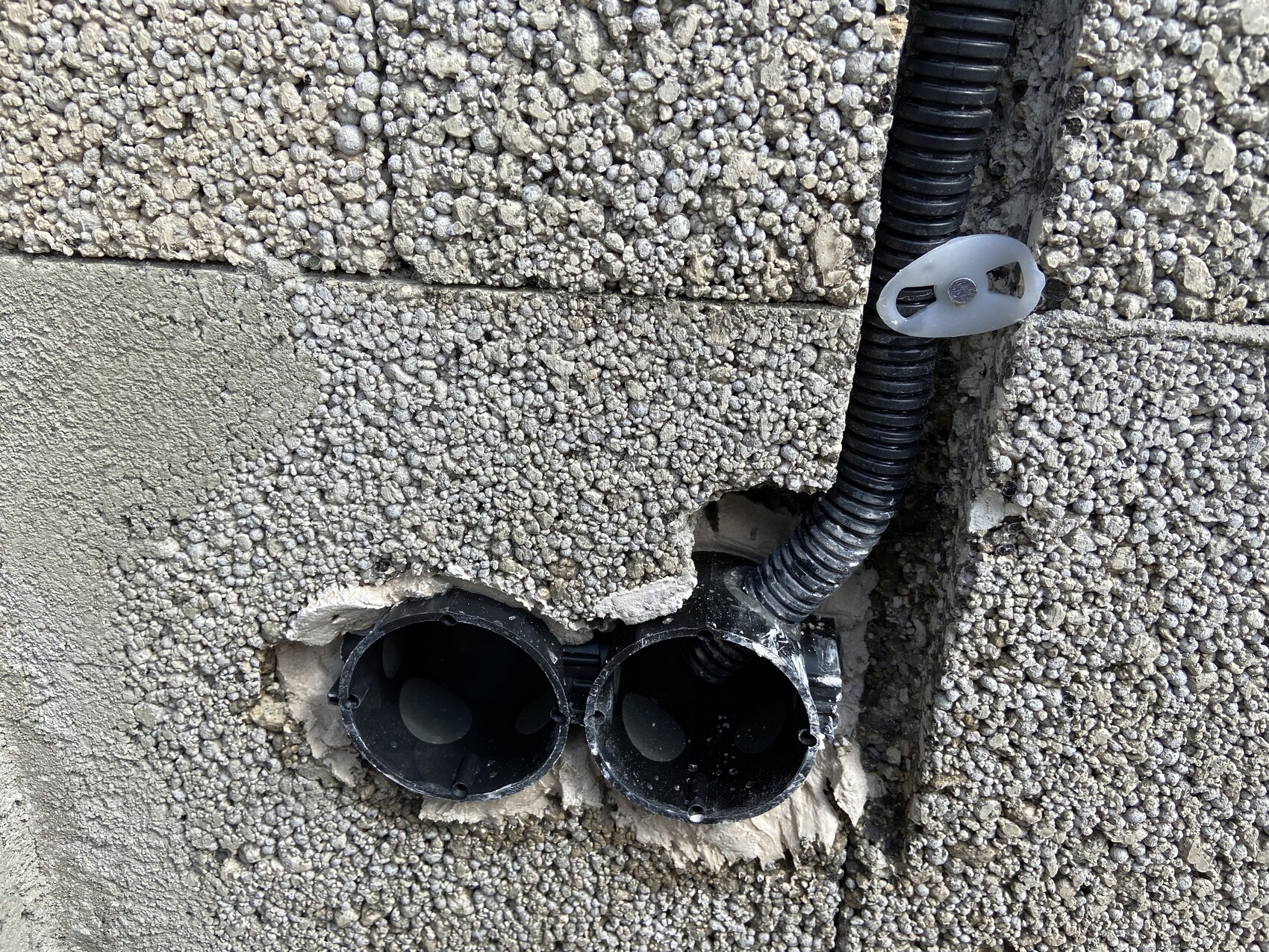Zwei schwarze runde Rohröffnungen in einer rauen Betonwand, daneben ein flexibler Kabelschlauch.