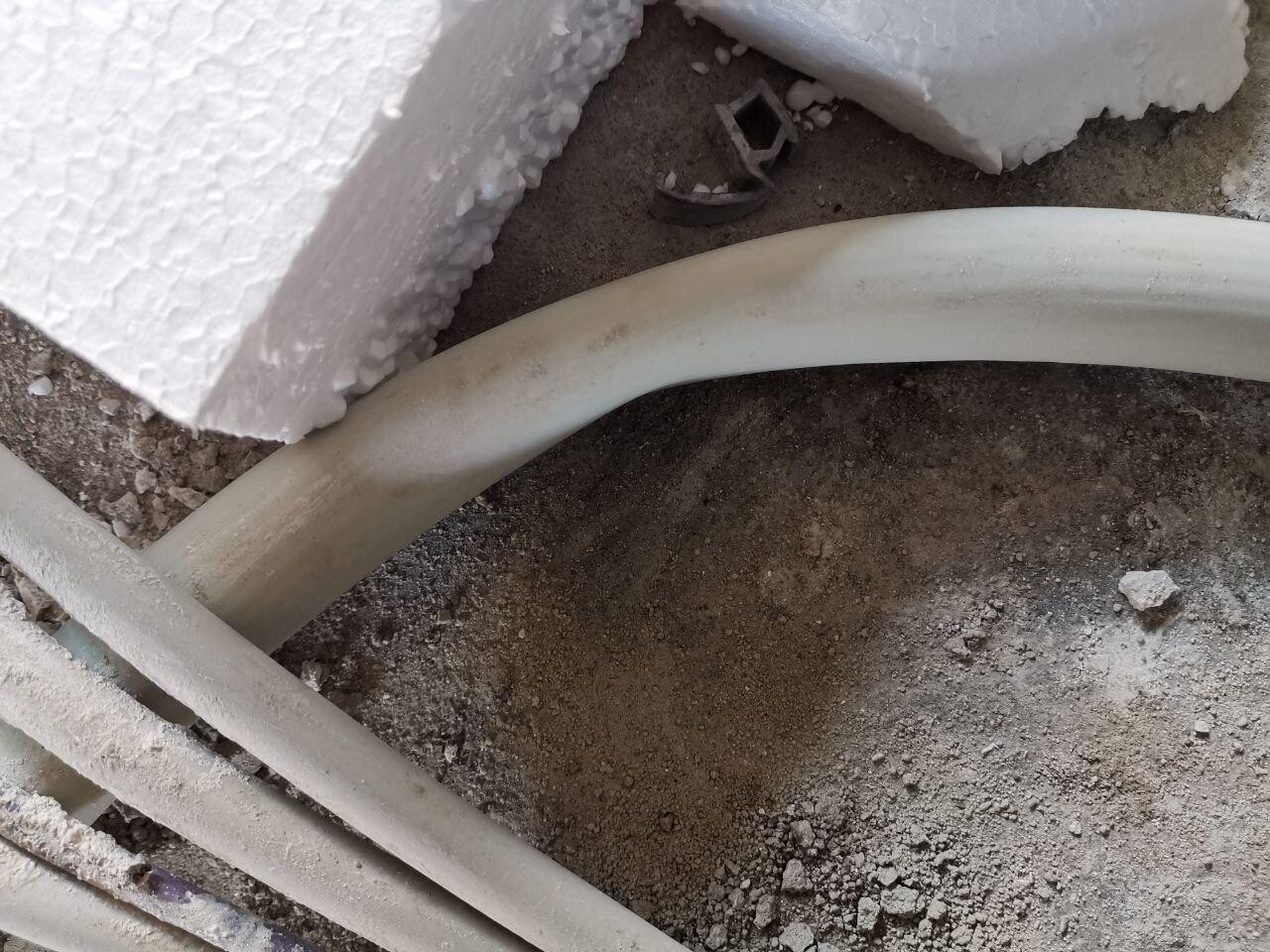Weißes, gebogenes PVC-Rohr liegt auf staubigem Boden neben Styropor-Brocken.