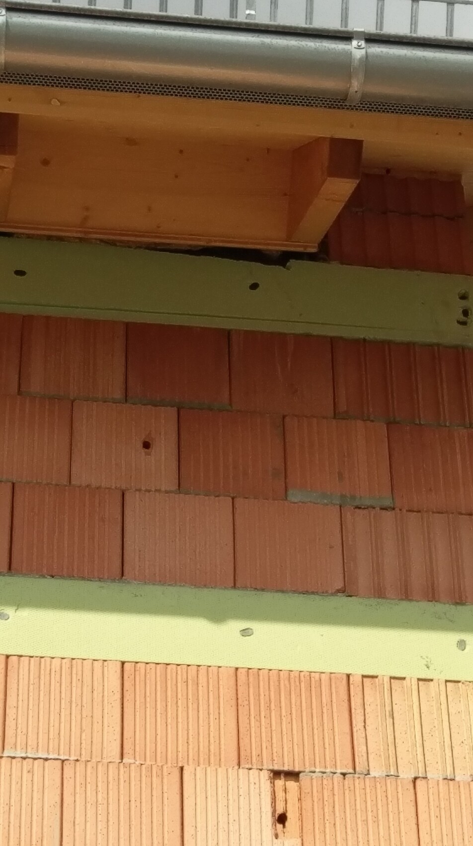 Baustellenaufnahme einer Rohbauwand aus roten Ziegelsteinen mit Holzbauteil und Metallrohr
