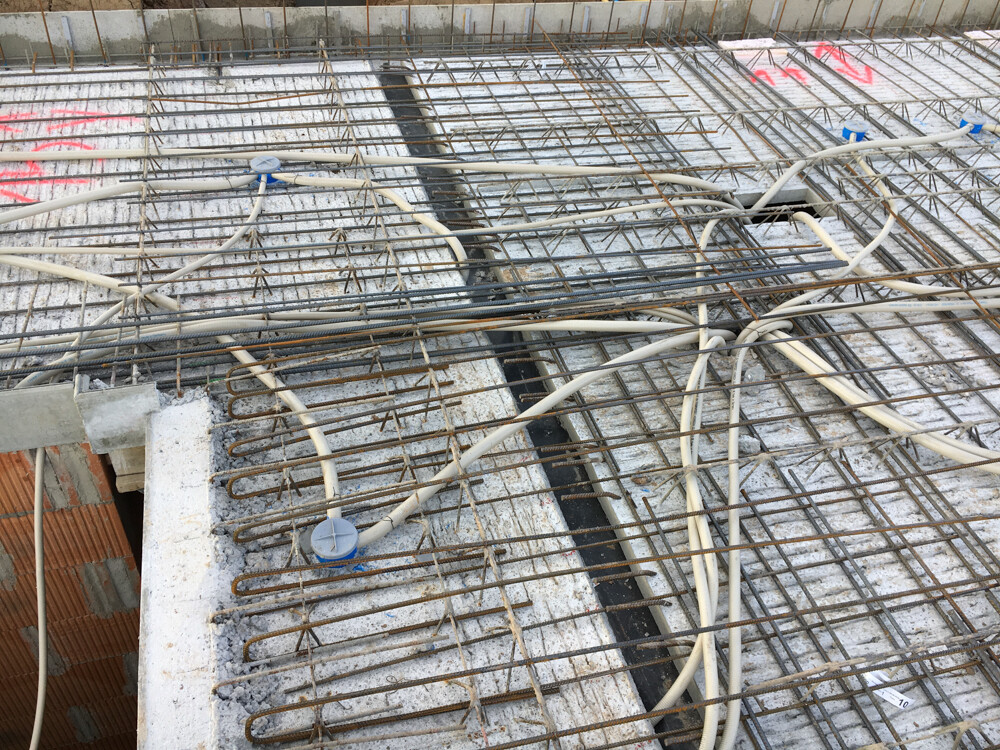 Baustelle: Stahl-Bewehrung, Kabel und Rohre auf Betonplatte.