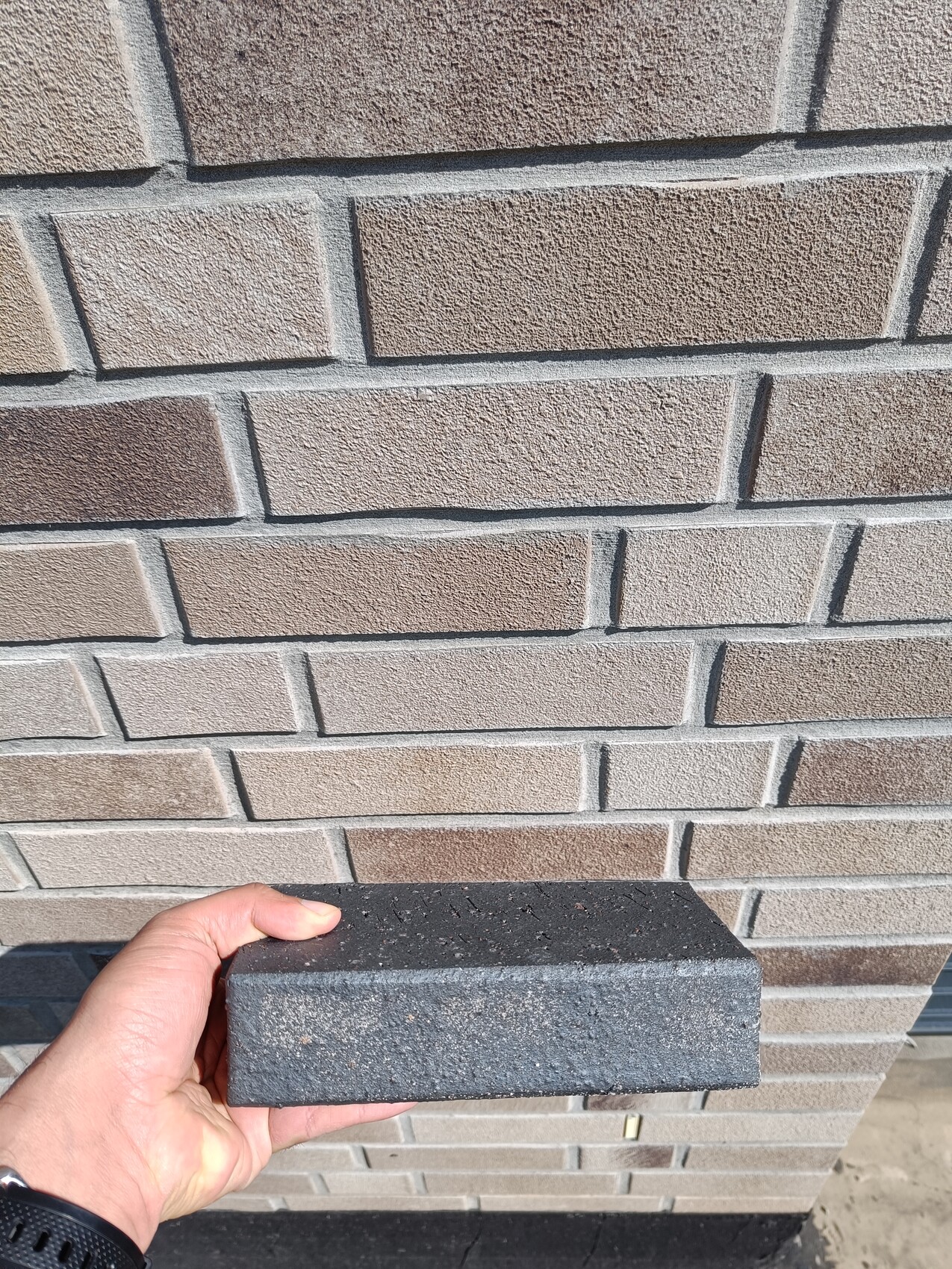 Person hält grauen Betonsteinblock vor beiger Ziegelwand