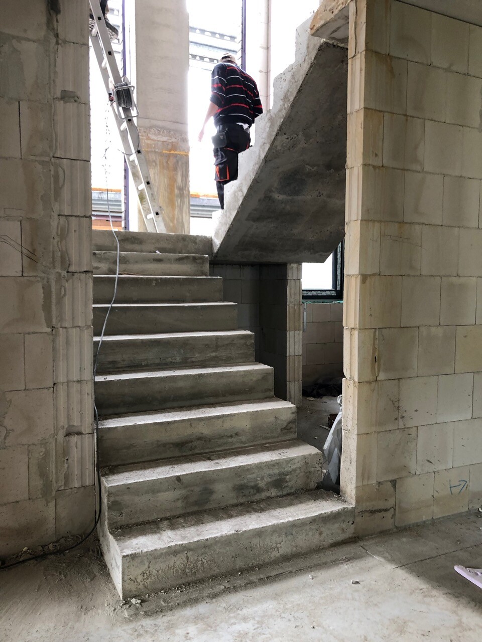 Baustelle – Mann in Arbeitskleidung steht oben auf einer Beton-Treppe in einem unfertigen Innenraum.