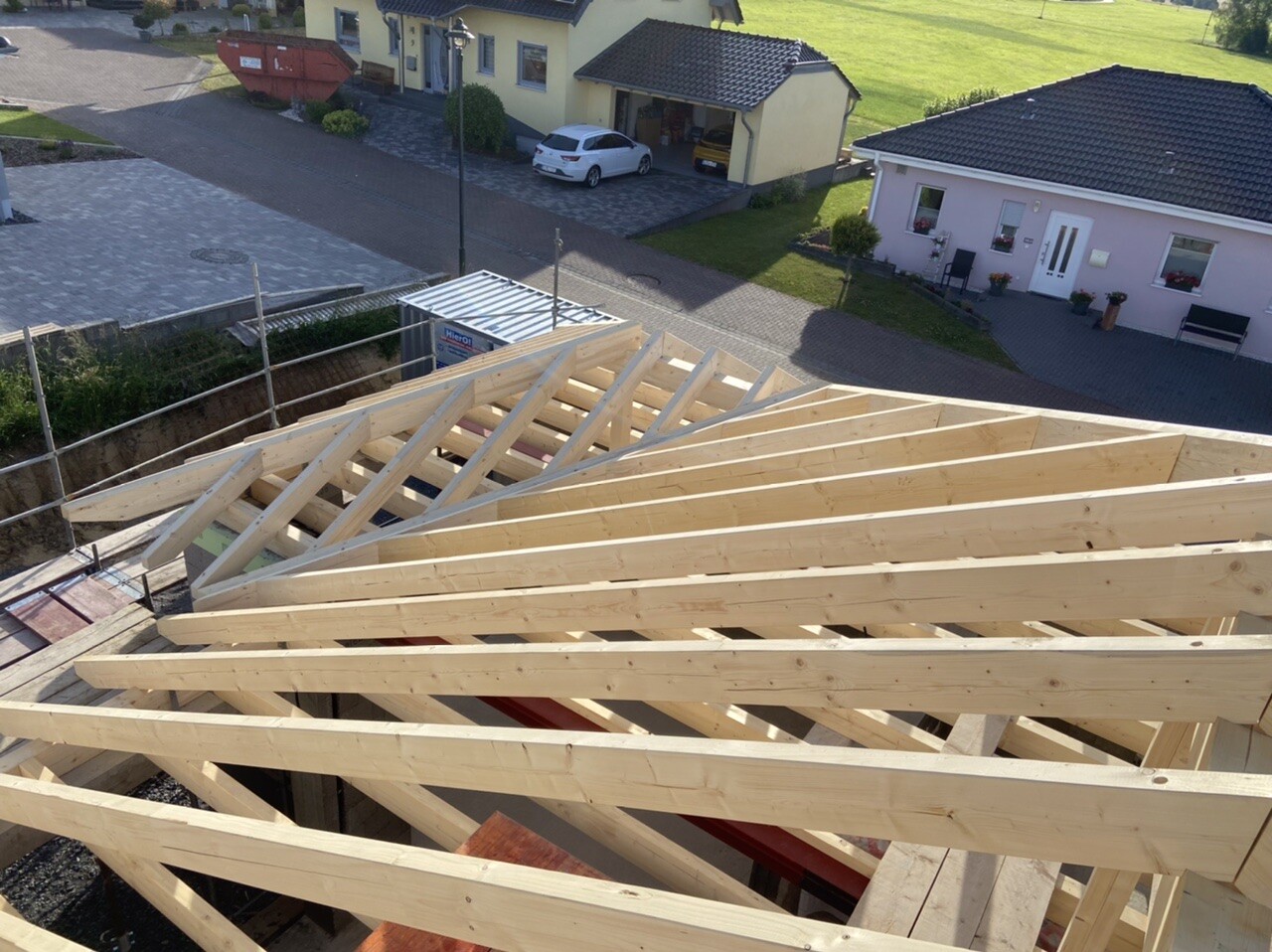 Holz-Dachstuhlrahmen eines Neubaus mit Baugerüst, Häuser im Hintergrund.