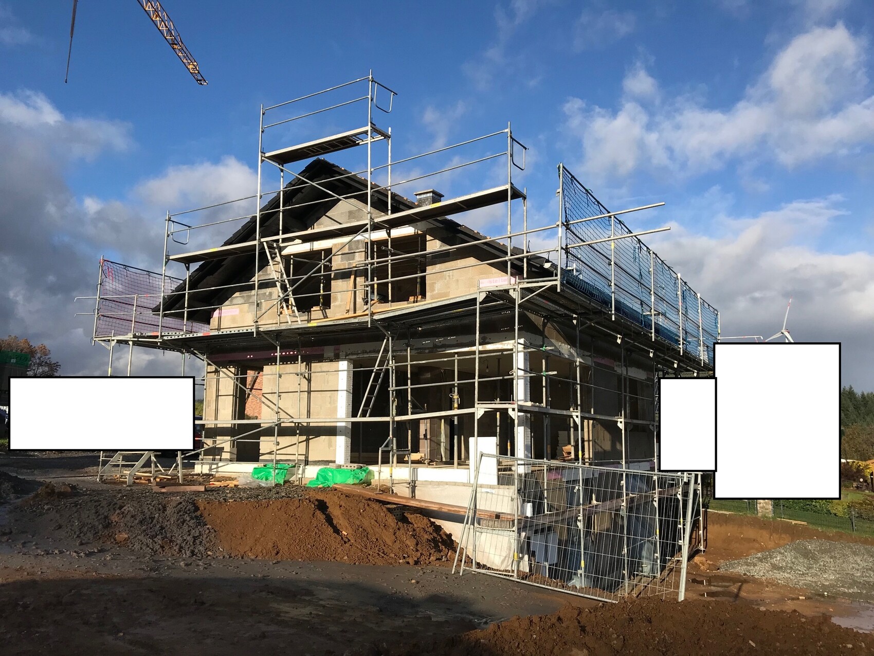 Neubau eines Hauses mit Gerüst, Bauzaun und Kran vor blauem Himmel.