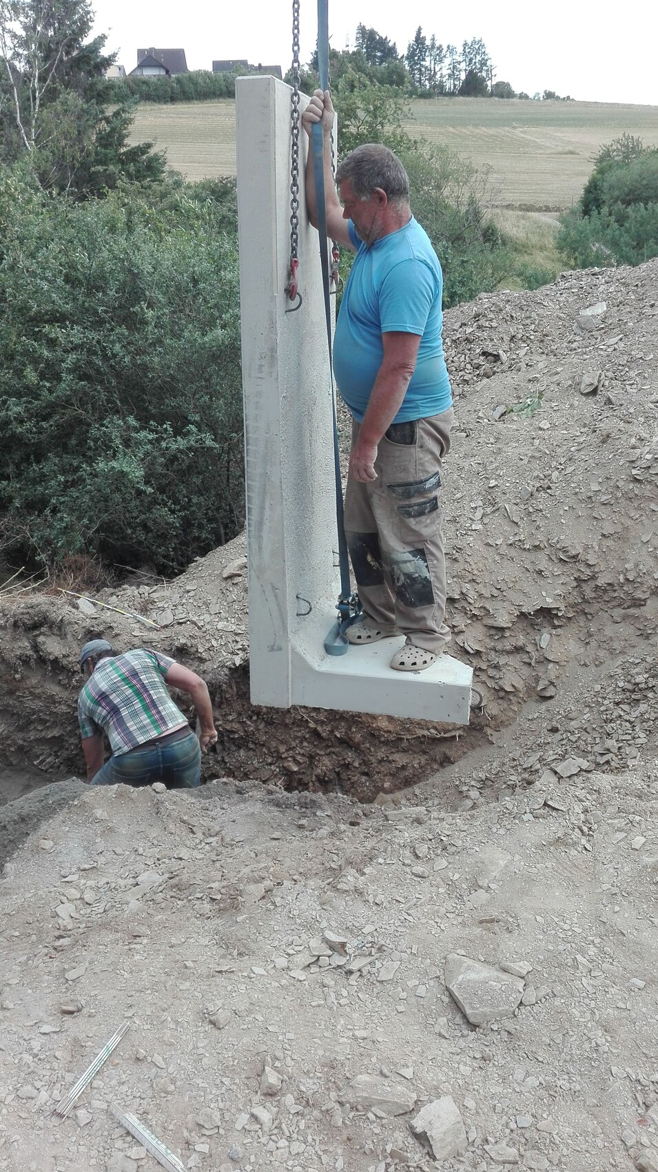 Zwei Bauarbeiter heben ein großes Betonbauteil in einer Baugrube.