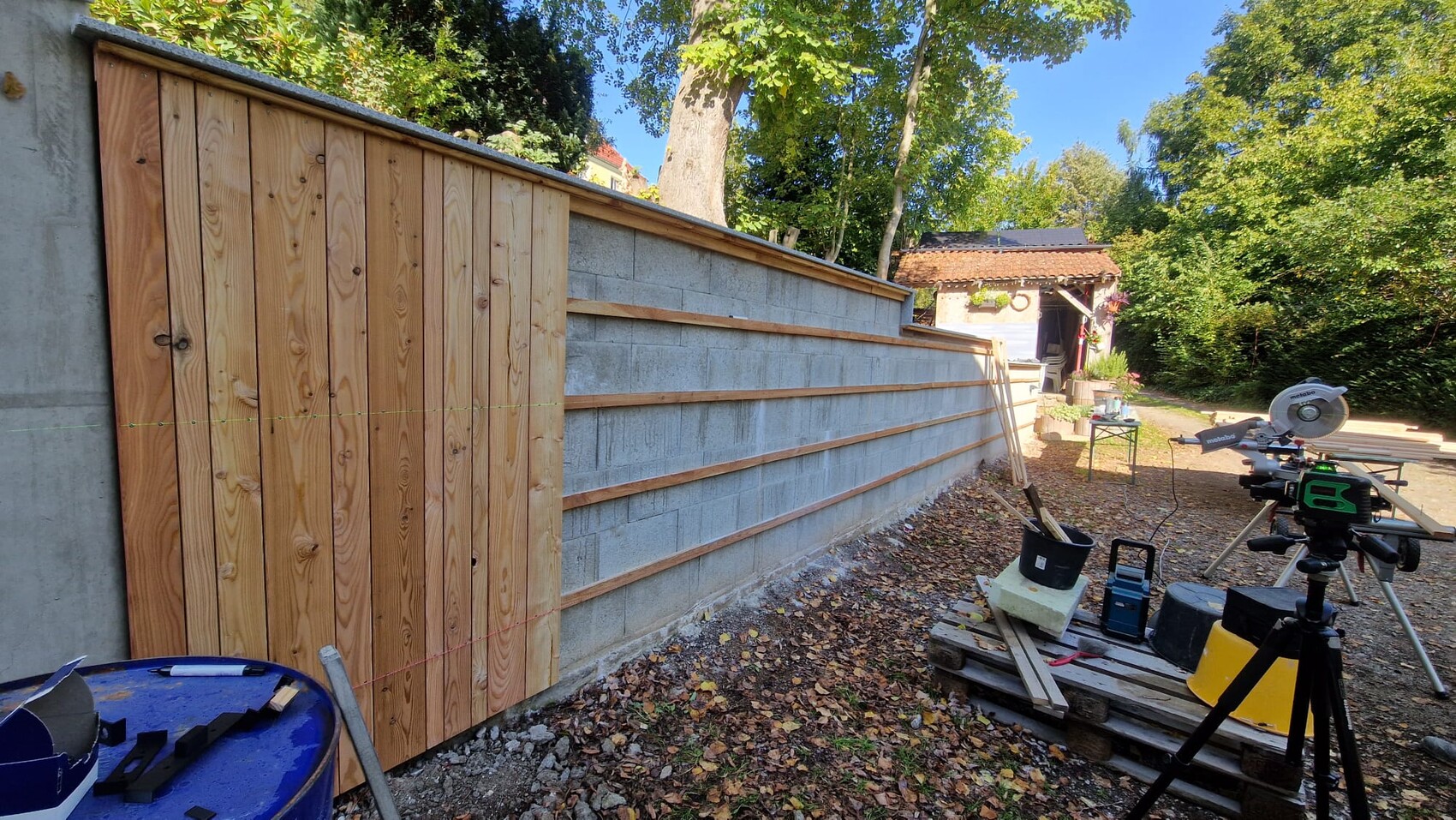 Baustelle mit Holzwandverkleidung an Betonmauer, Werkzeuge und Säge im Freien