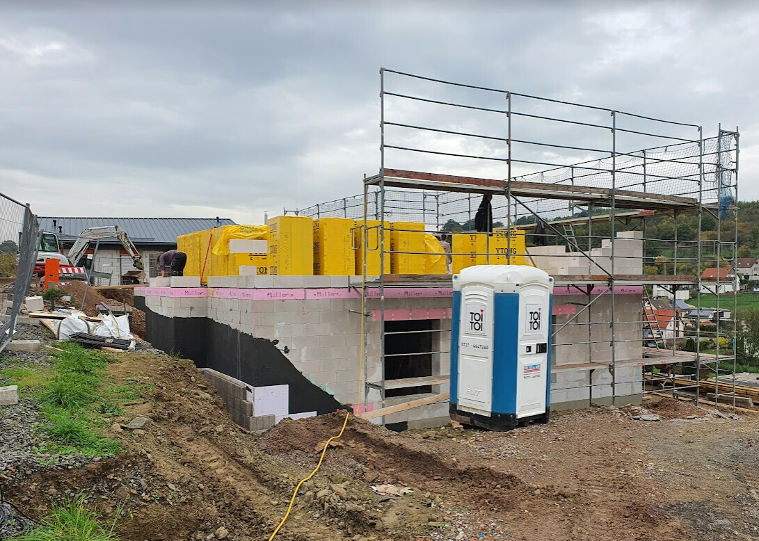 Rohbau-Baustelle mit Gerüst, gelben Dämmplatten und Toi-Toi-WC.