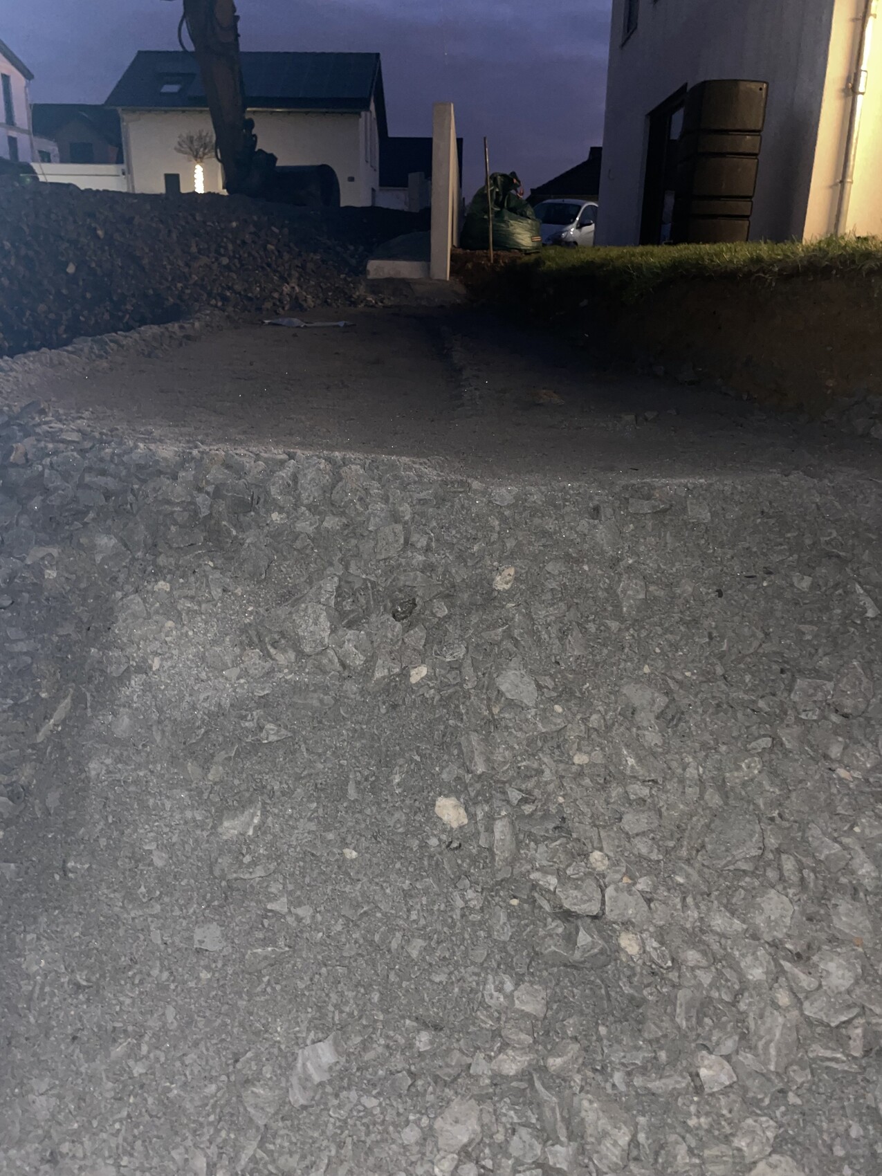 Baufläche mit grobem Kies und Erde, Bauarbeiten am Hintergrund bei Abendlicht