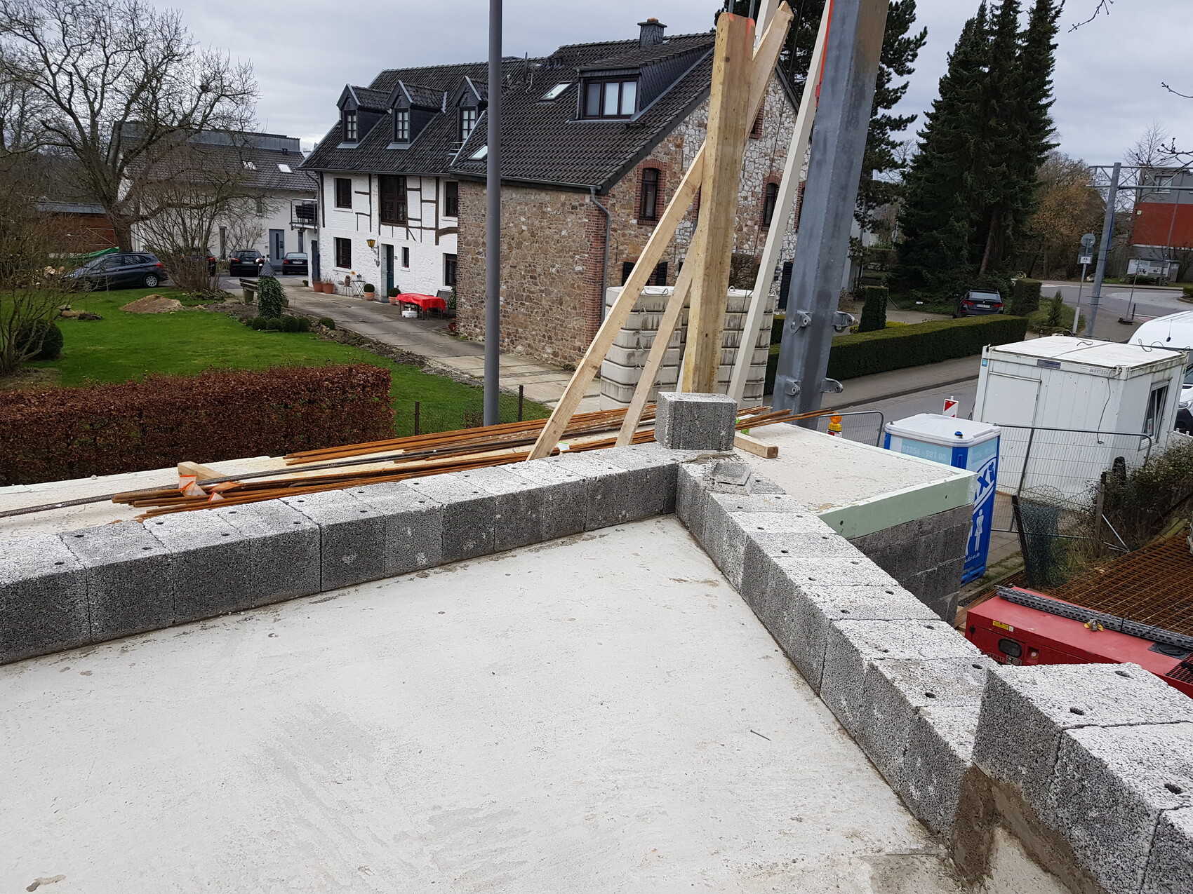 Rohbau-Dach mit Betonblöcken, Holzlatten und Werkzeug; Wohnhäuser im Hintergrund