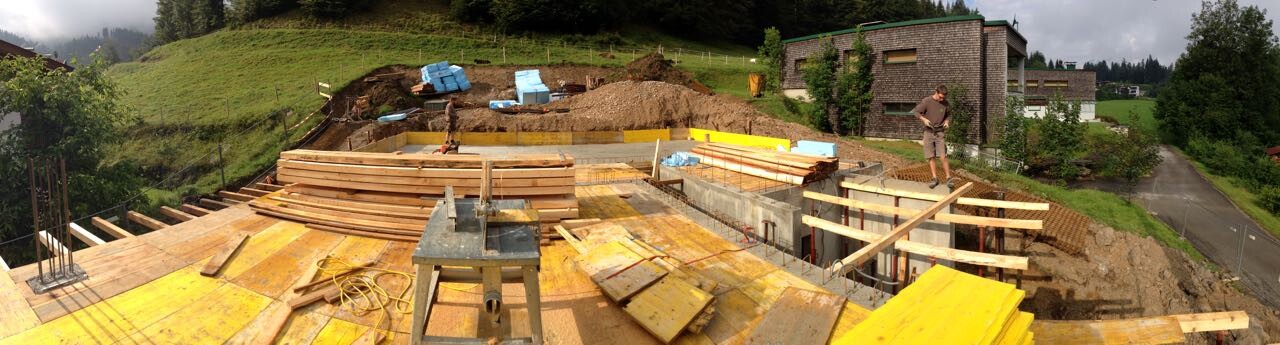 Baustelle mit Holzbalken, Betonfundament und Bauarbeiter auf offener Baustelle