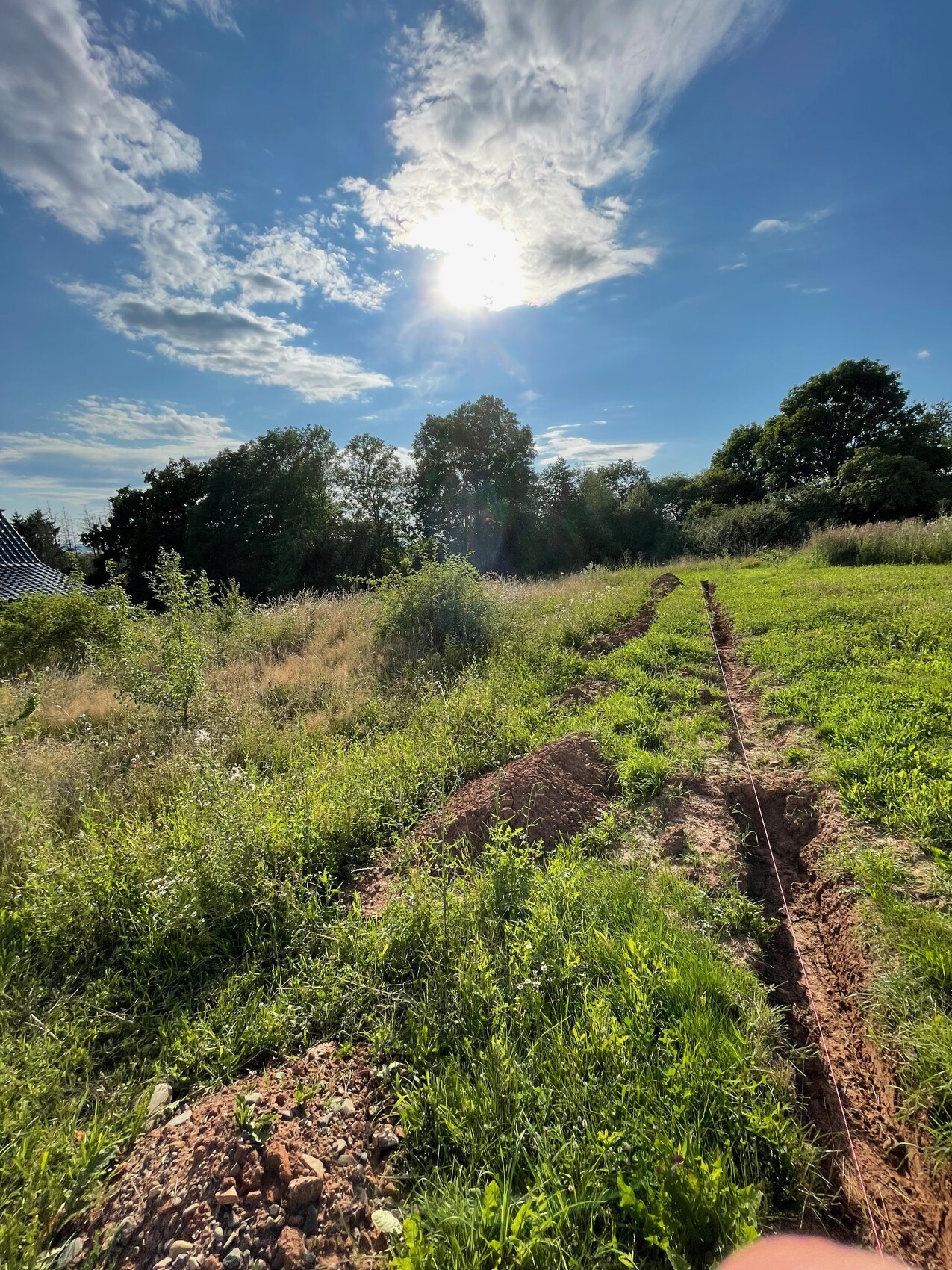 Baugrundstück mit Graben für Fundament, Gras und Bäume unter sonnigem Himmel