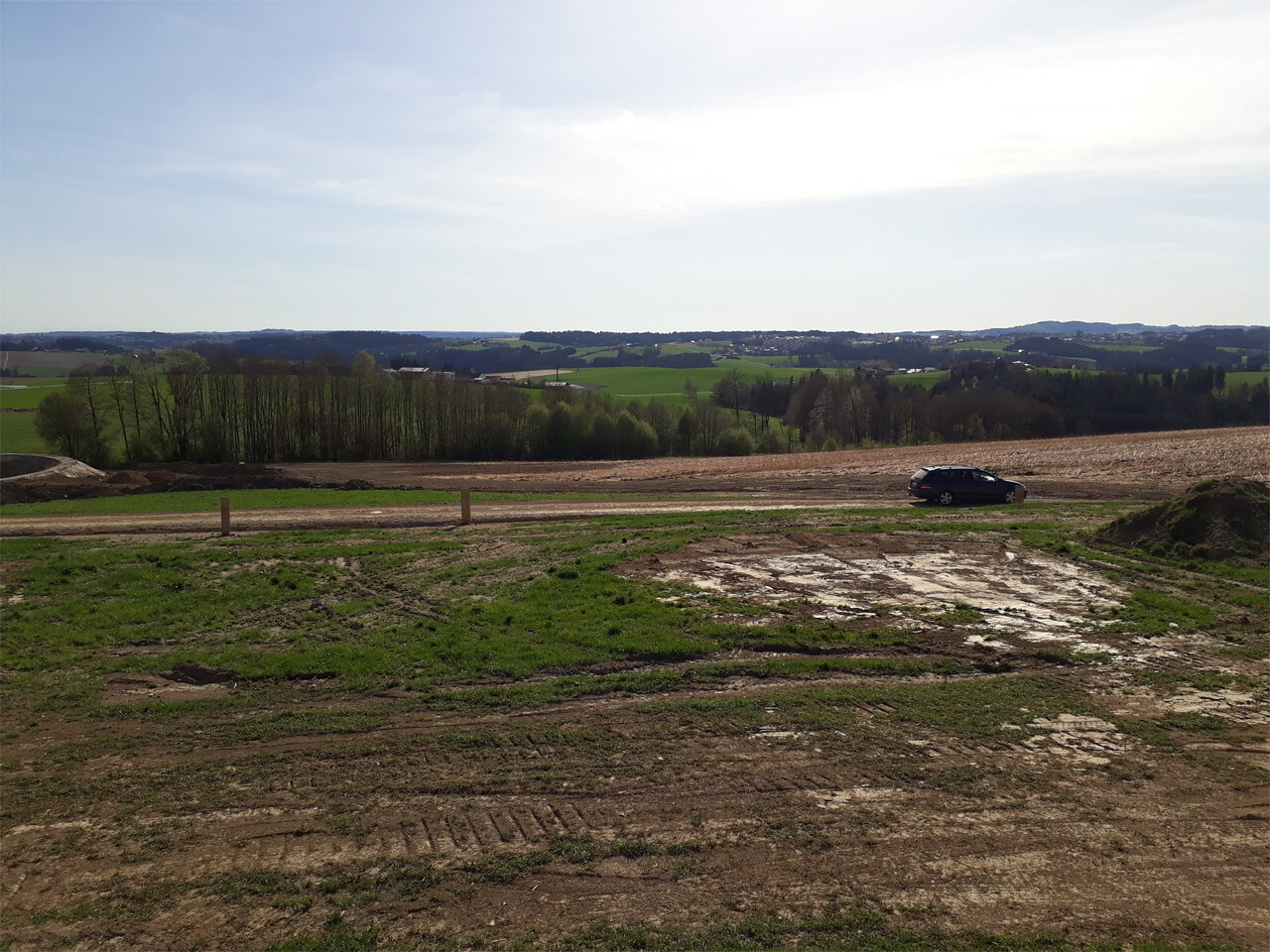 Baustelle auf freiem Feld mit Erde, Reifenabdrücken und Auto am Rand