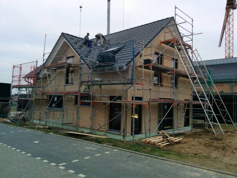 Zweistöckiges Haus im Rohbau mit Gerüst, Dacharbeiten und Bauarbeitern auf dem Dach.