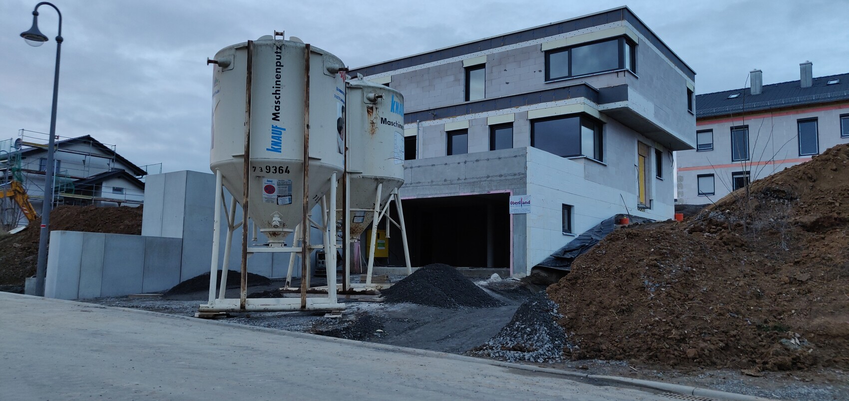 Baustelle mit zwei Betonmischern vor unfertigem Wohngebäude, Erde und Kies.