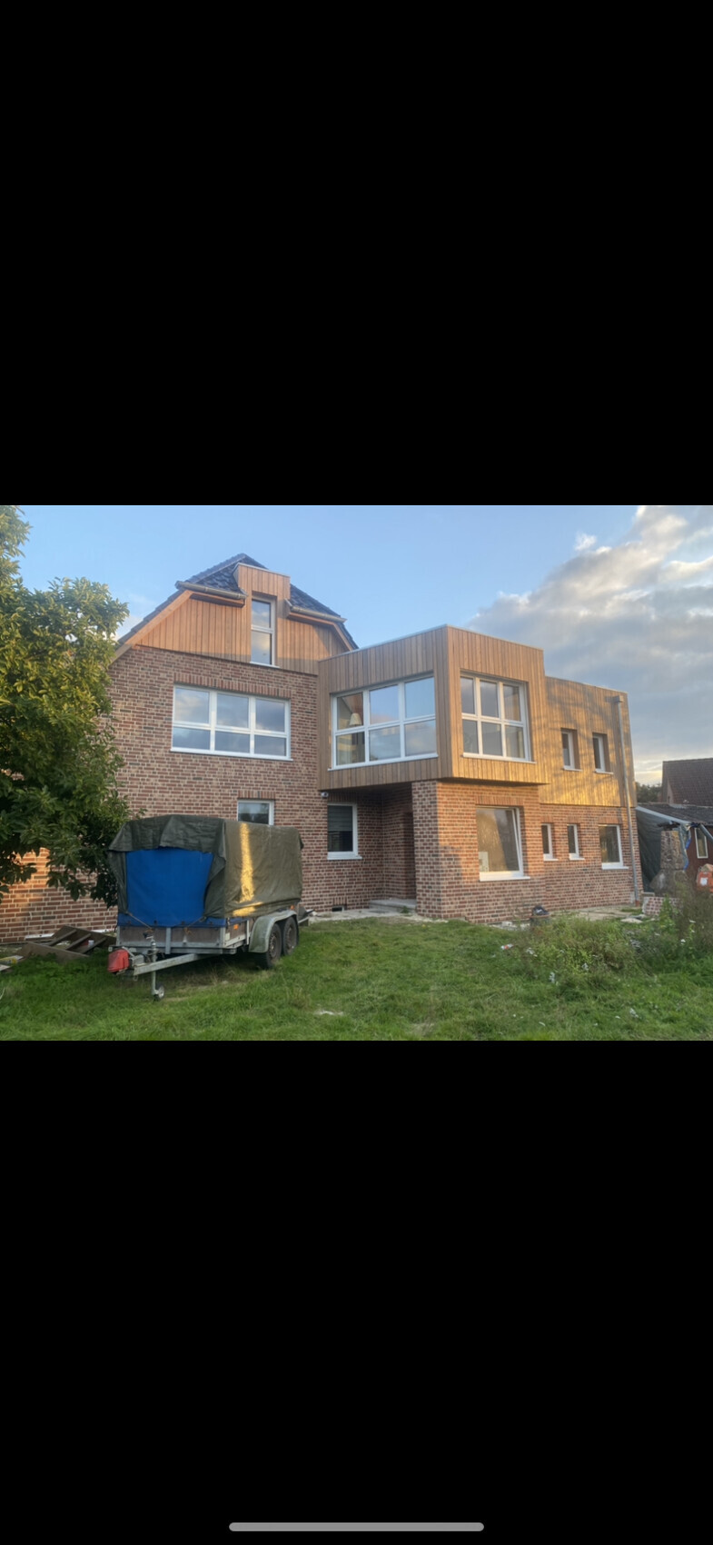 Mehrfamilienhaus mit Backstein- und Holzfassade; Baustelle mit Bauwagen im Vorgarten.