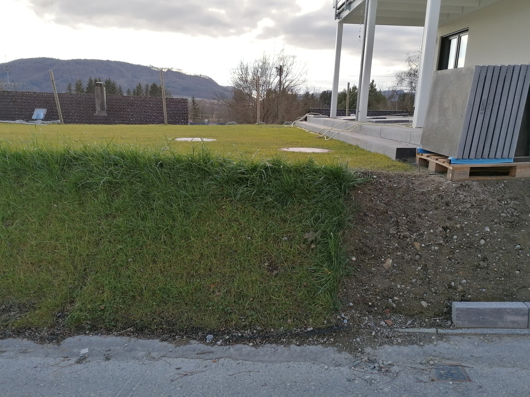 Außenbereich einer Neubau-Baustelle mit Graswall, Fundament und Baumaterialien am Haus