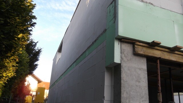 Aussenwand-Rohbau mit gruenen Daemmplatten und Baugeruest auf Baustelle
