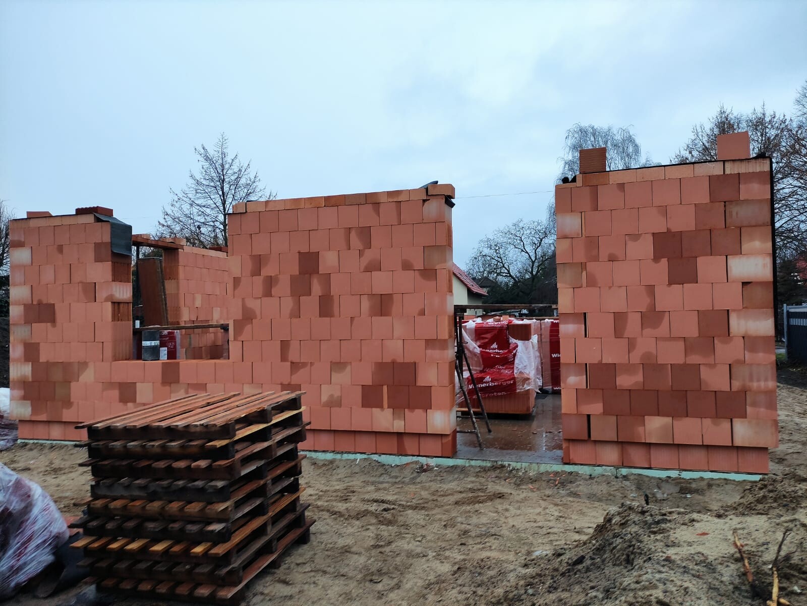 Baufeld mit roten Ziegelwänden, offener Durchgang, Paletten davor, Bauwerk im Rohzustand.
