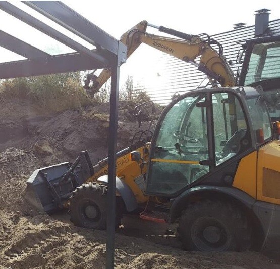 Gelber Bagger mit Ausleger neben Stahlrahmen auf einer Sandbaustelle.