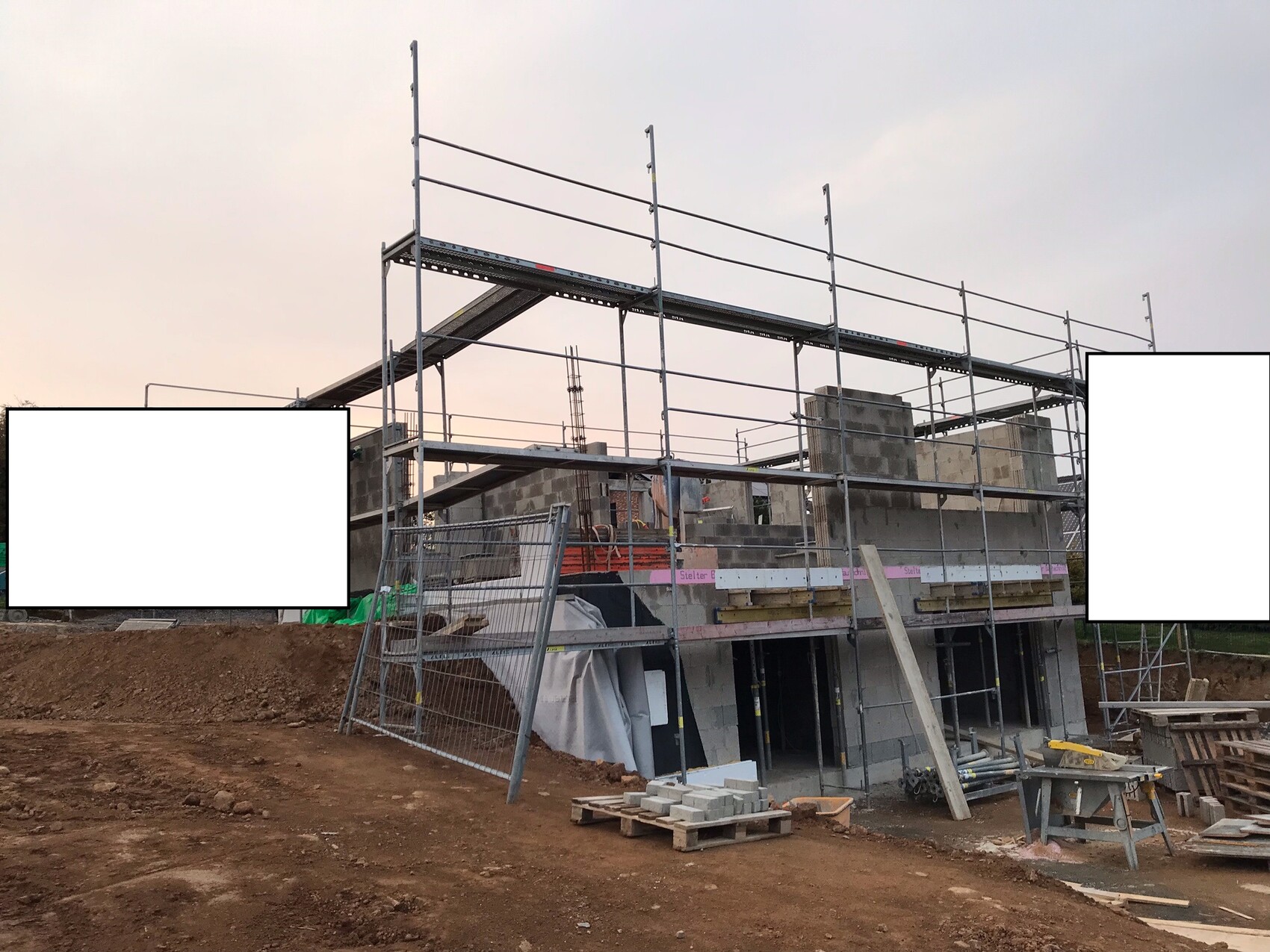 Baustelle mit Stahlgerüst um einen halbfertigen Betonrohbau; Erdarbeiten und Materialien.